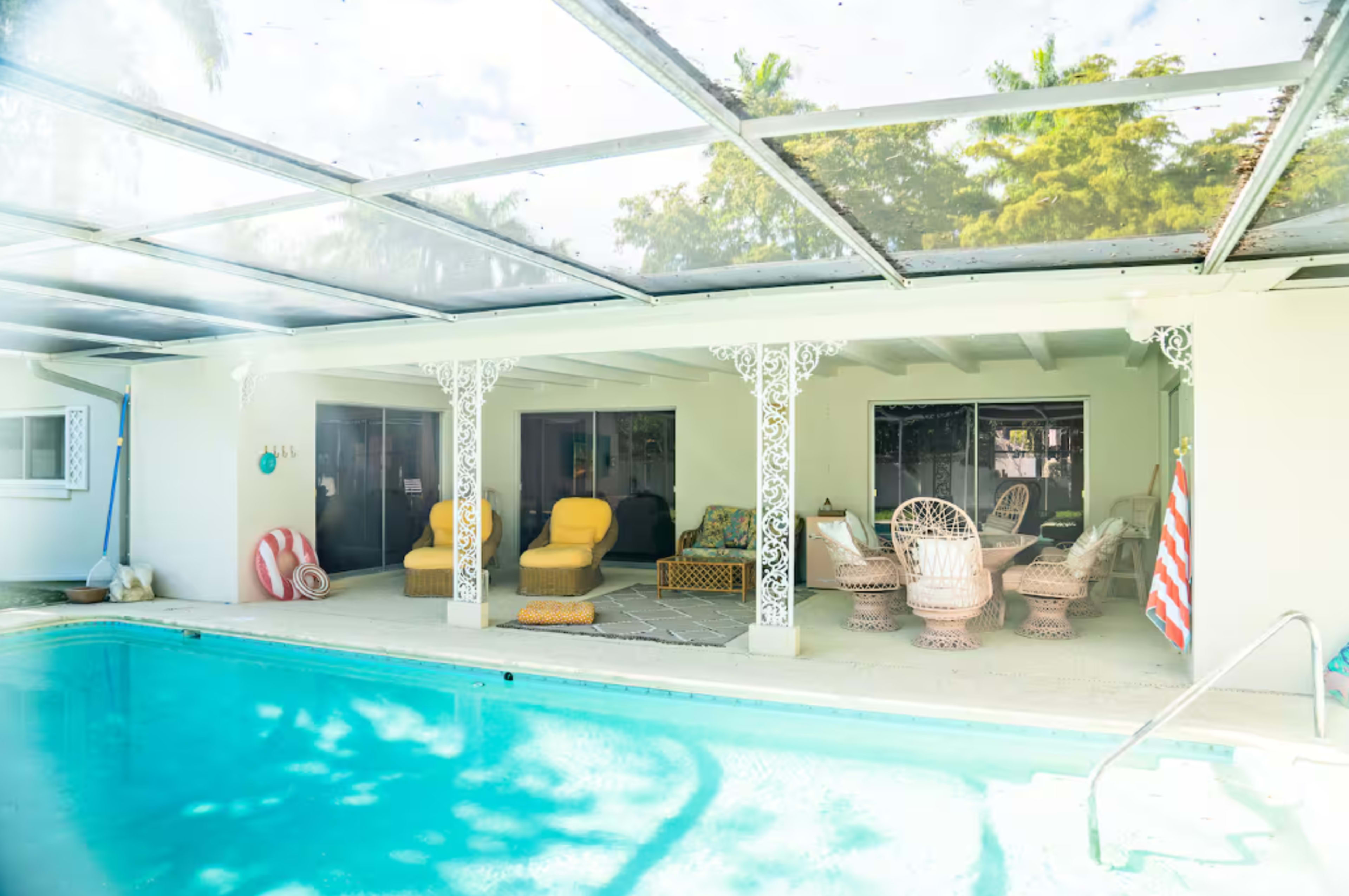 The image shows a pool area with a covered patio featuring several chairs and tables beside a blue swimming pool.