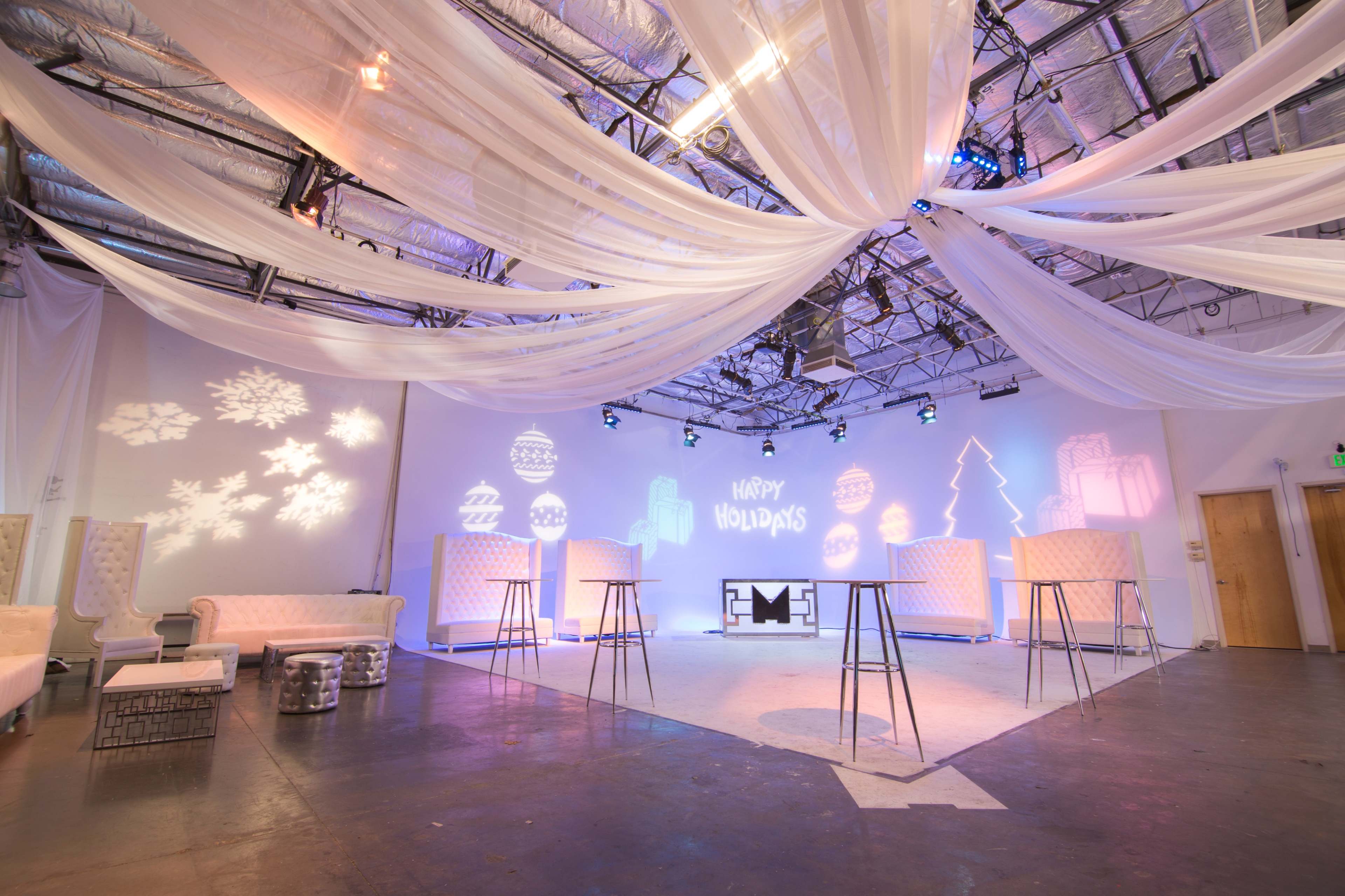 A festive indoor event space decorated with draped fabric, colorful lighting, and holiday-themed projections on the walls.