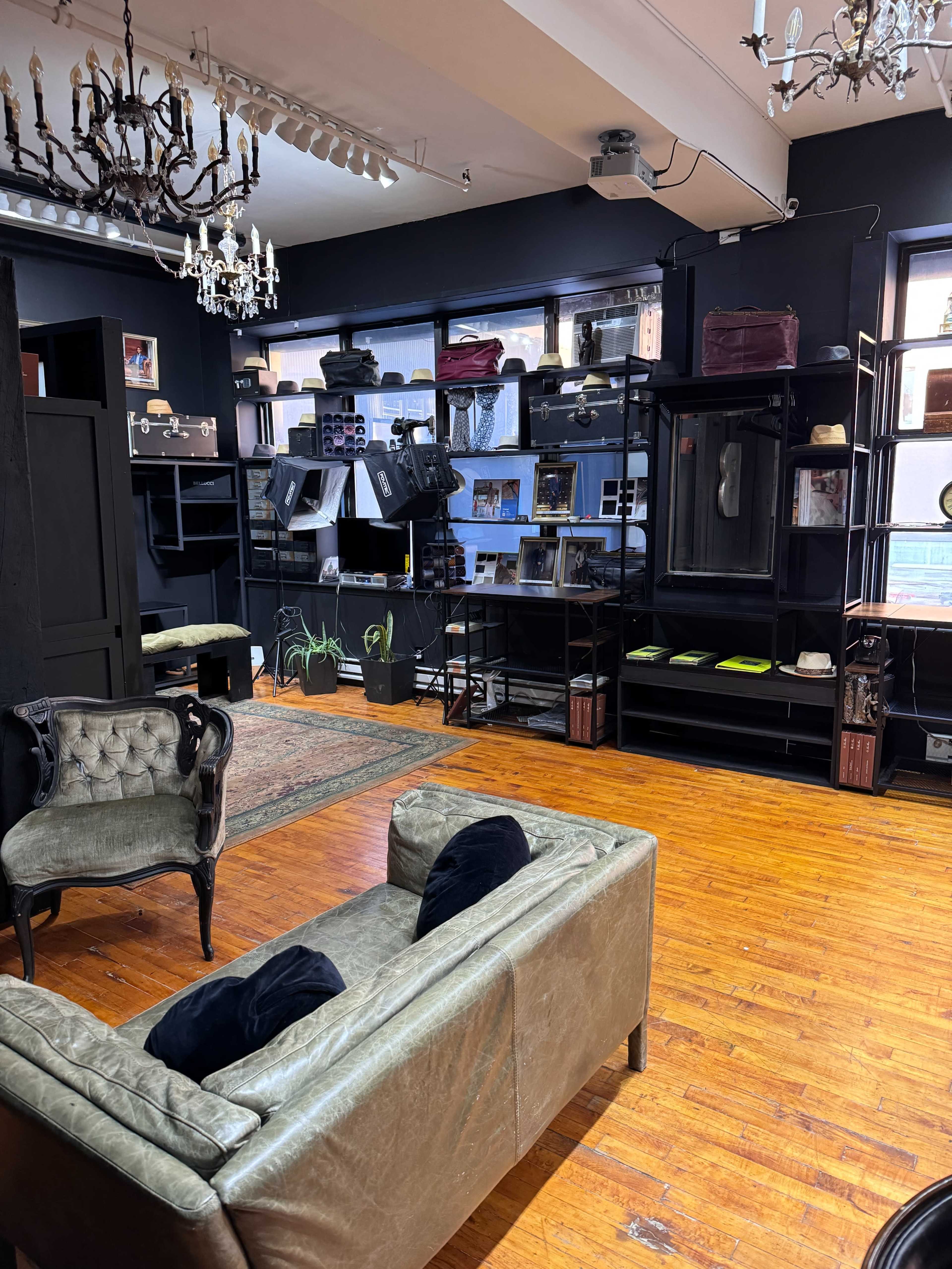 An eclectic interior space with dark walls, wooden floors, various shelves displaying items, and vintage furniture including a green sofa and a chandelier.