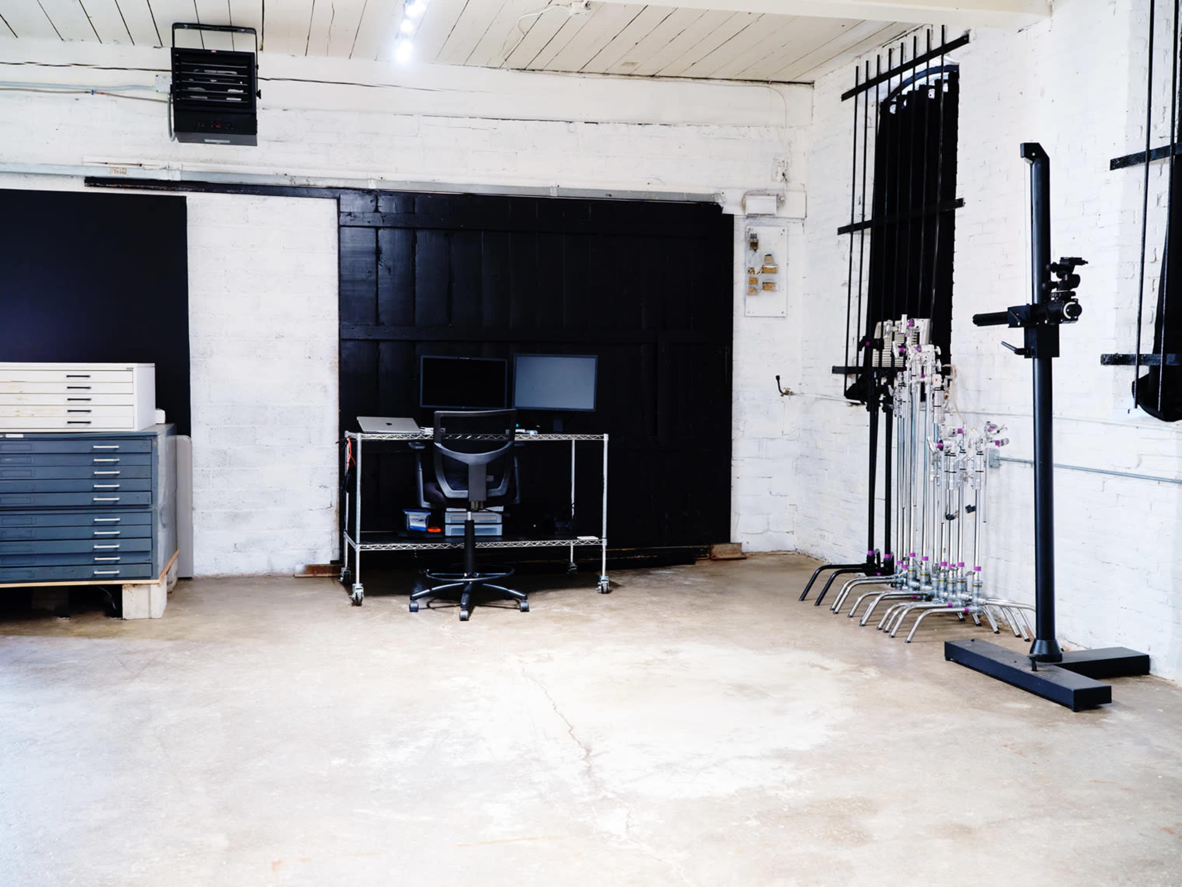 The image shows a spacious, empty room featuring a desk with a computer and a chair, along with various equipment on the walls and floor.