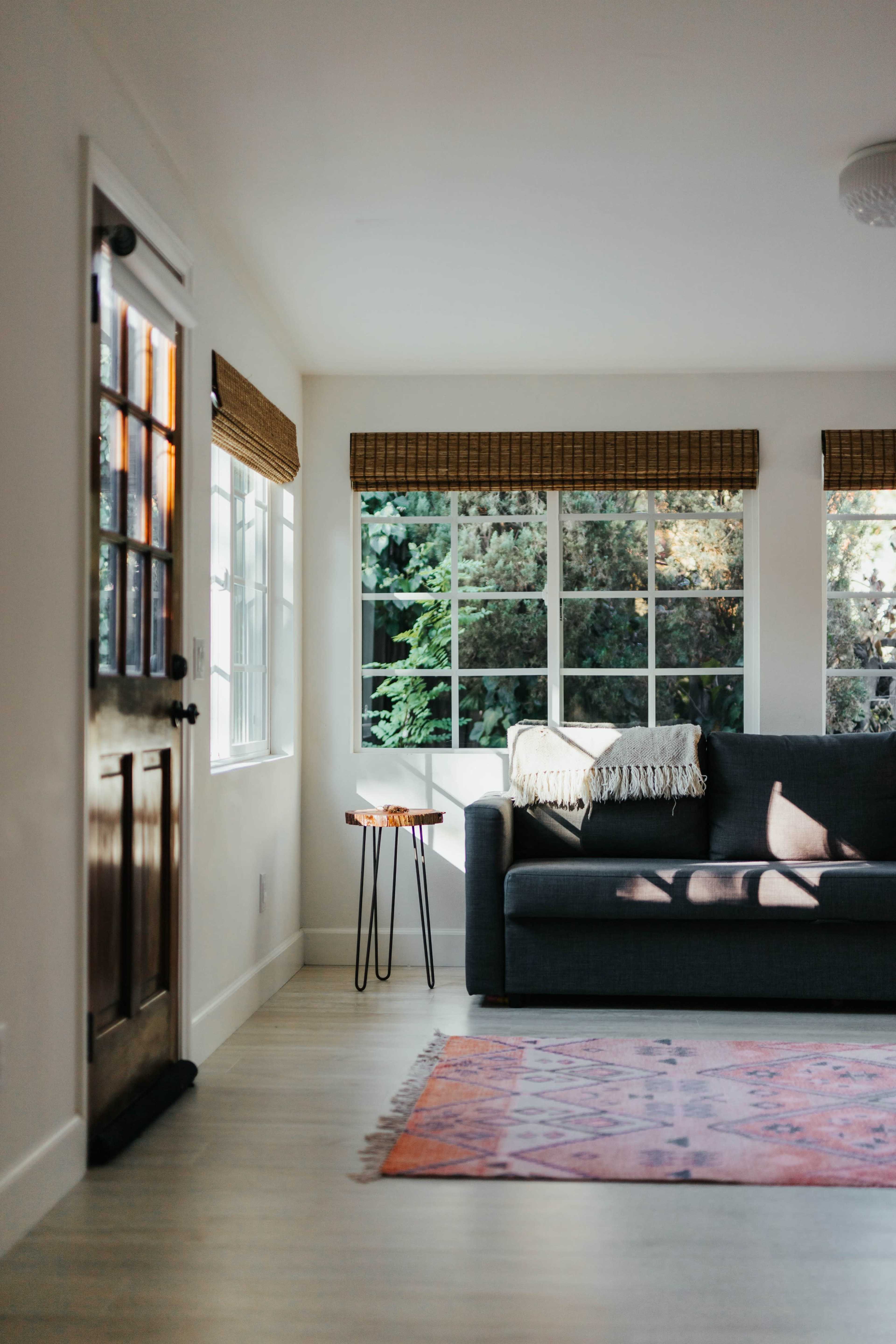 A neatly arranged living room features a gray sofa, a small side table, and large windows allowing natural light to illuminate the space.