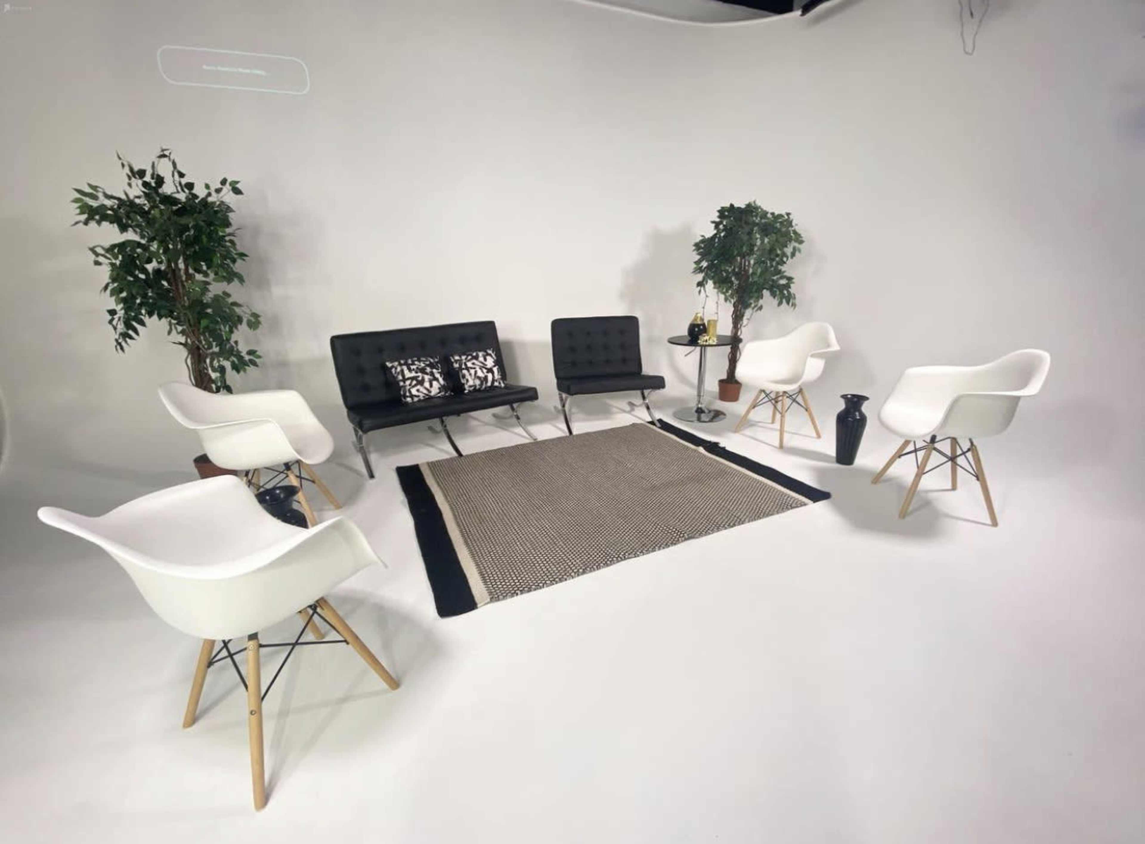 A minimalist waiting area with black and white furniture, including a sofa, chairs, and a rug, set against a plain white backdrop.
