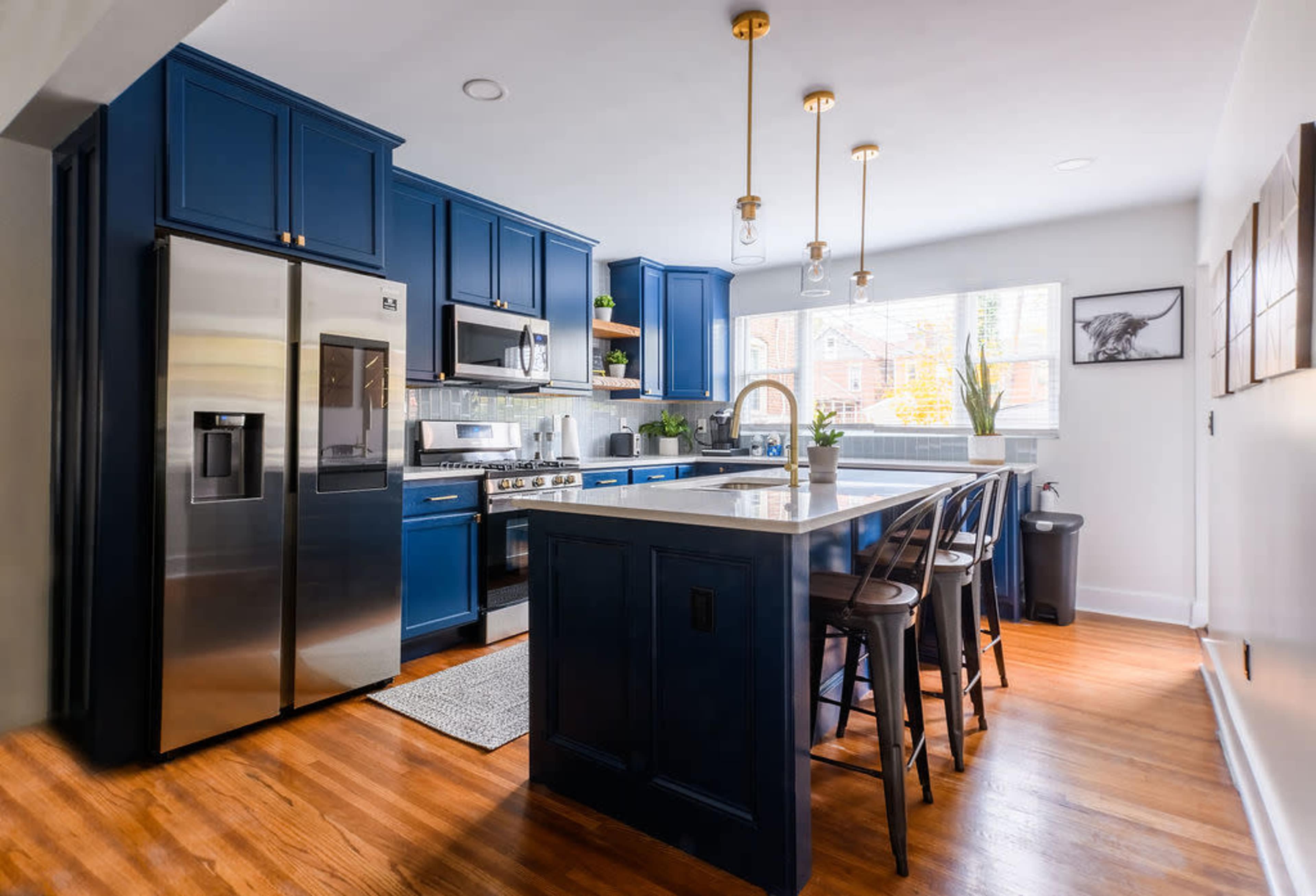 A modern kitchen featuring blue cabinetry, stainless steel appliances, a central island with seating, and natural light streaming in from a window.