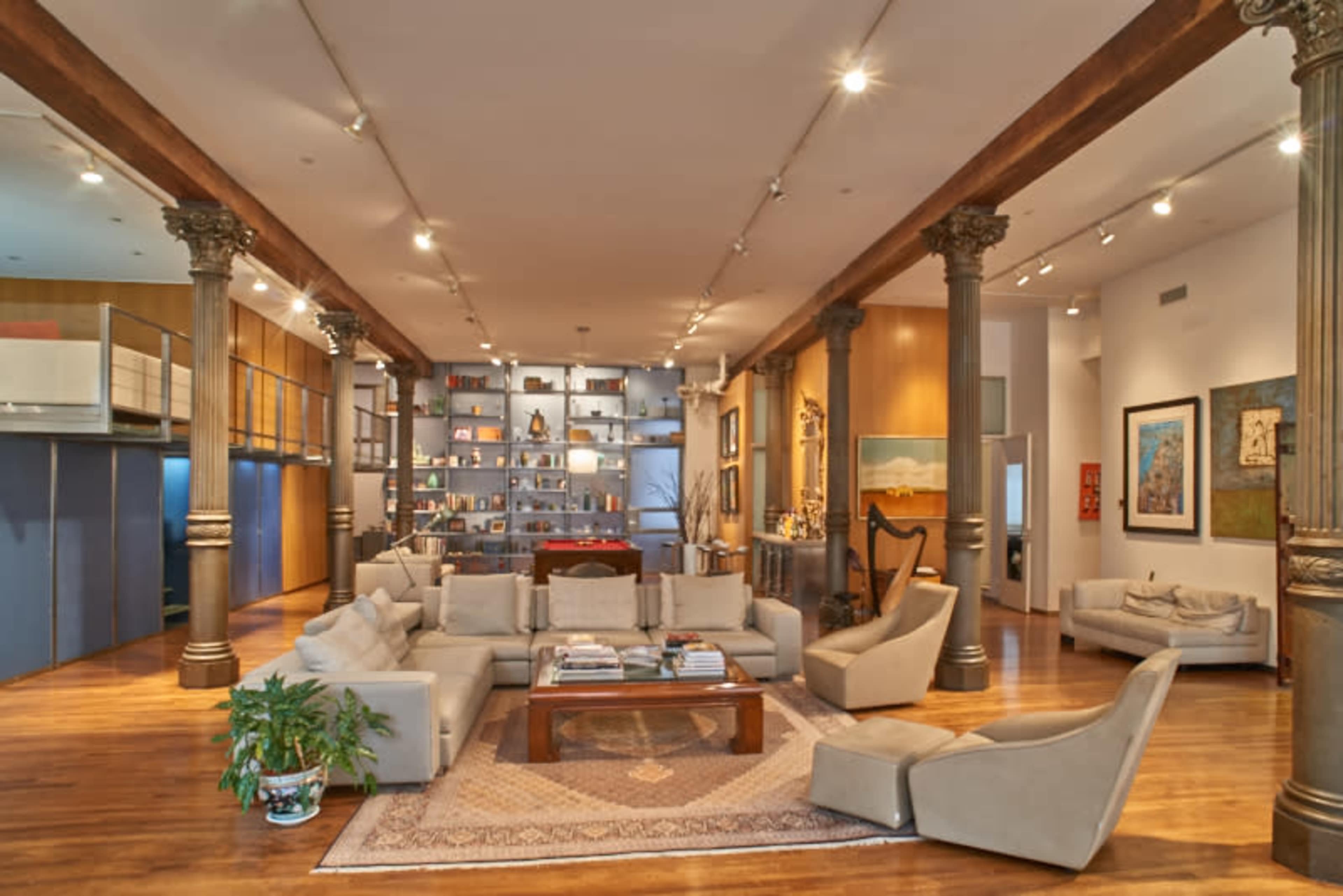 A spacious living room with a sectional sofa, a coffee table, columns, and bookshelves filled with various items along the walls.