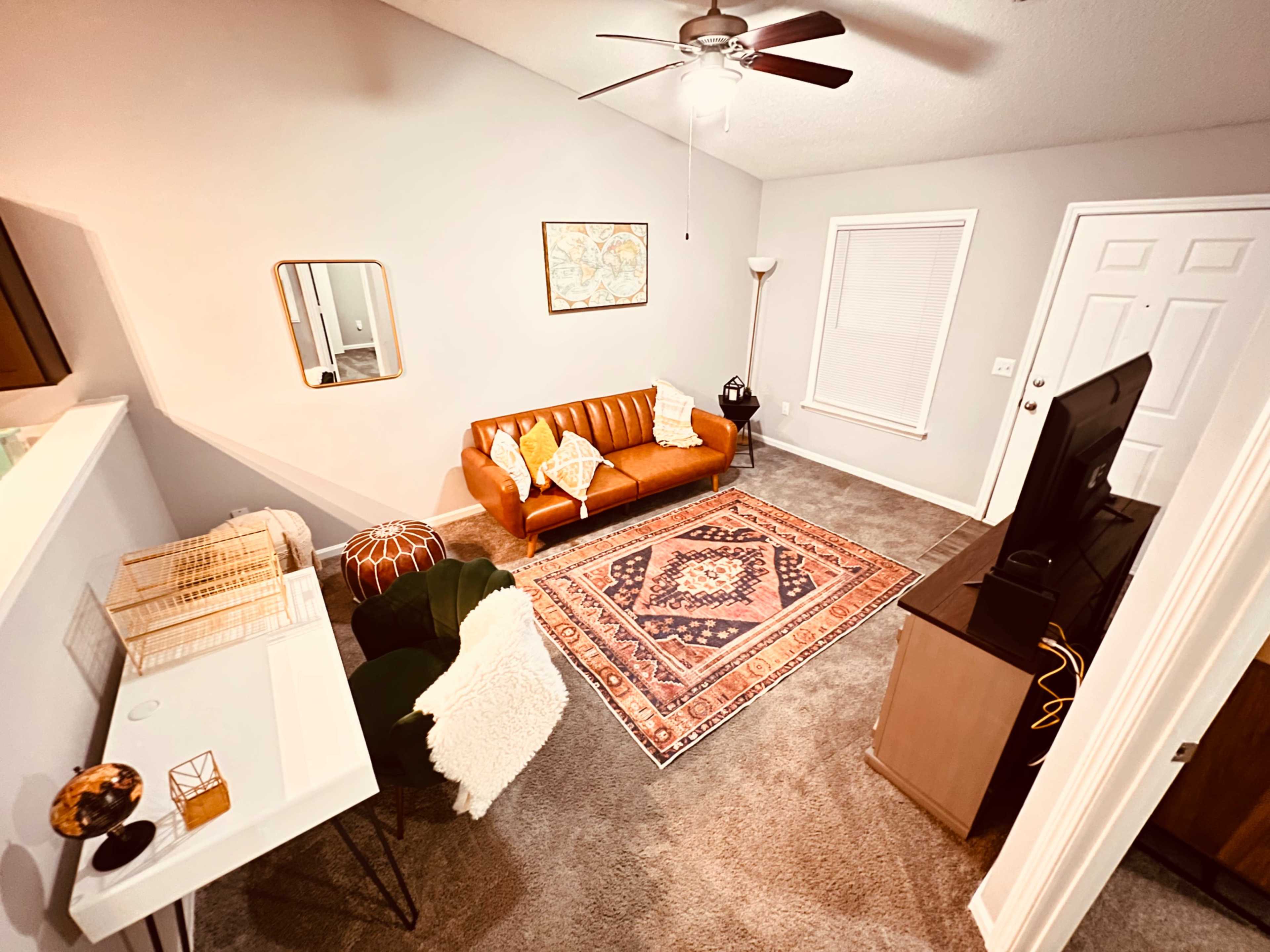 A cozy living room with a brown leather sofa, a patterned area rug, and a television, complemented by a floor lamp and decorative elements.