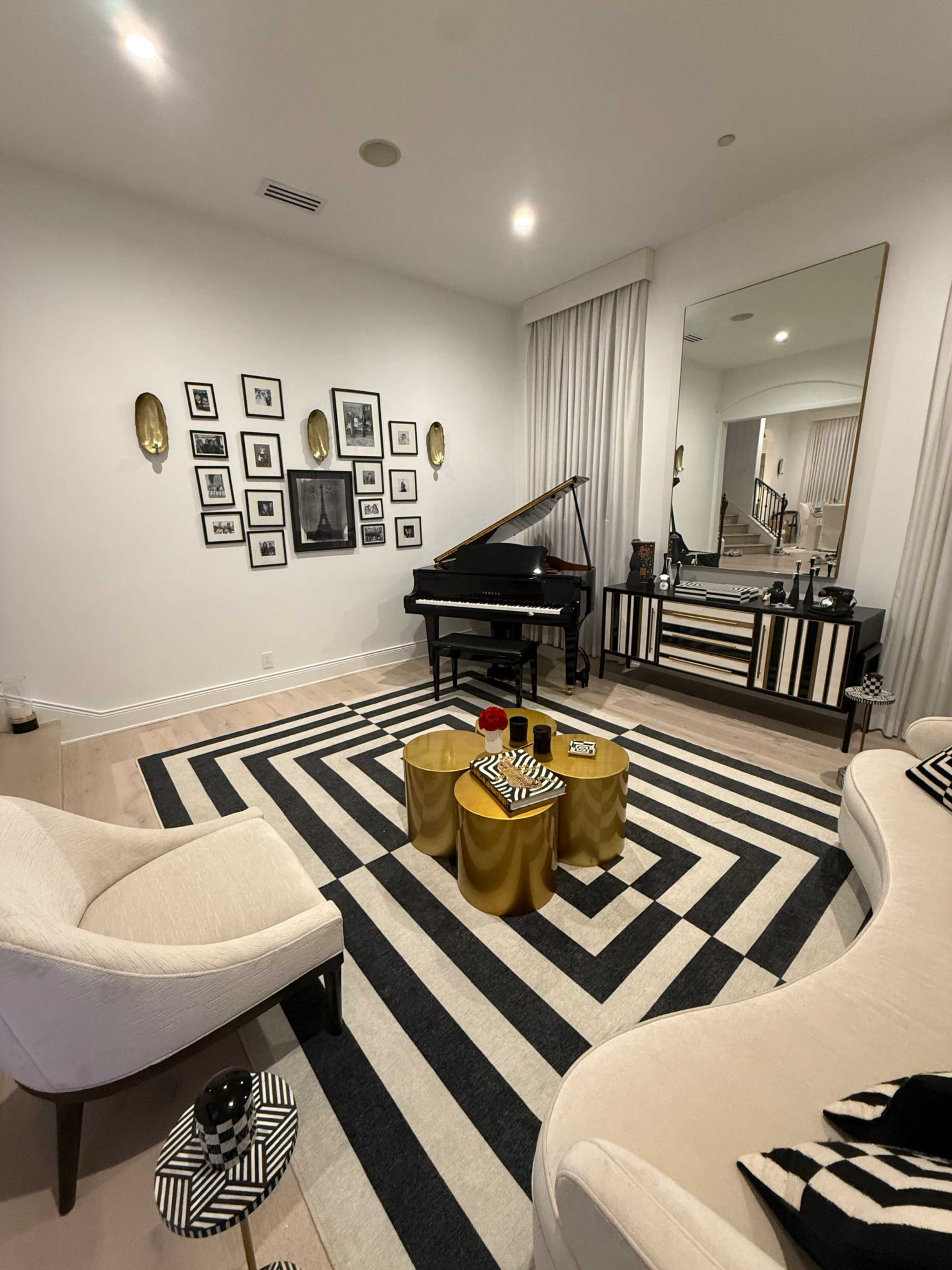 The image depicts a modern living room featuring a grand piano, a striped area rug, and a coffee table with gold and black accents, complemented by framed black-and-white photographs on the wall.