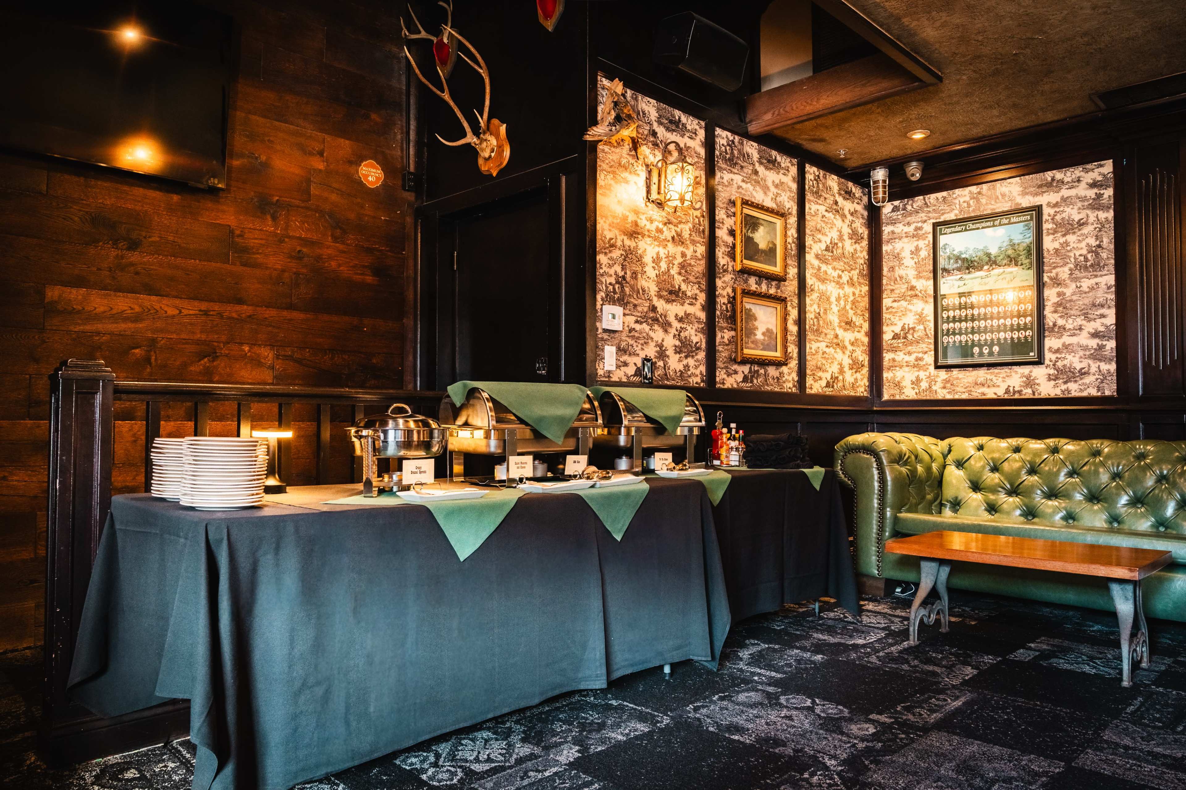 A darkly decorated restaurant interior features a buffet table with warming trays and a green tufted couch against a patterned wall.