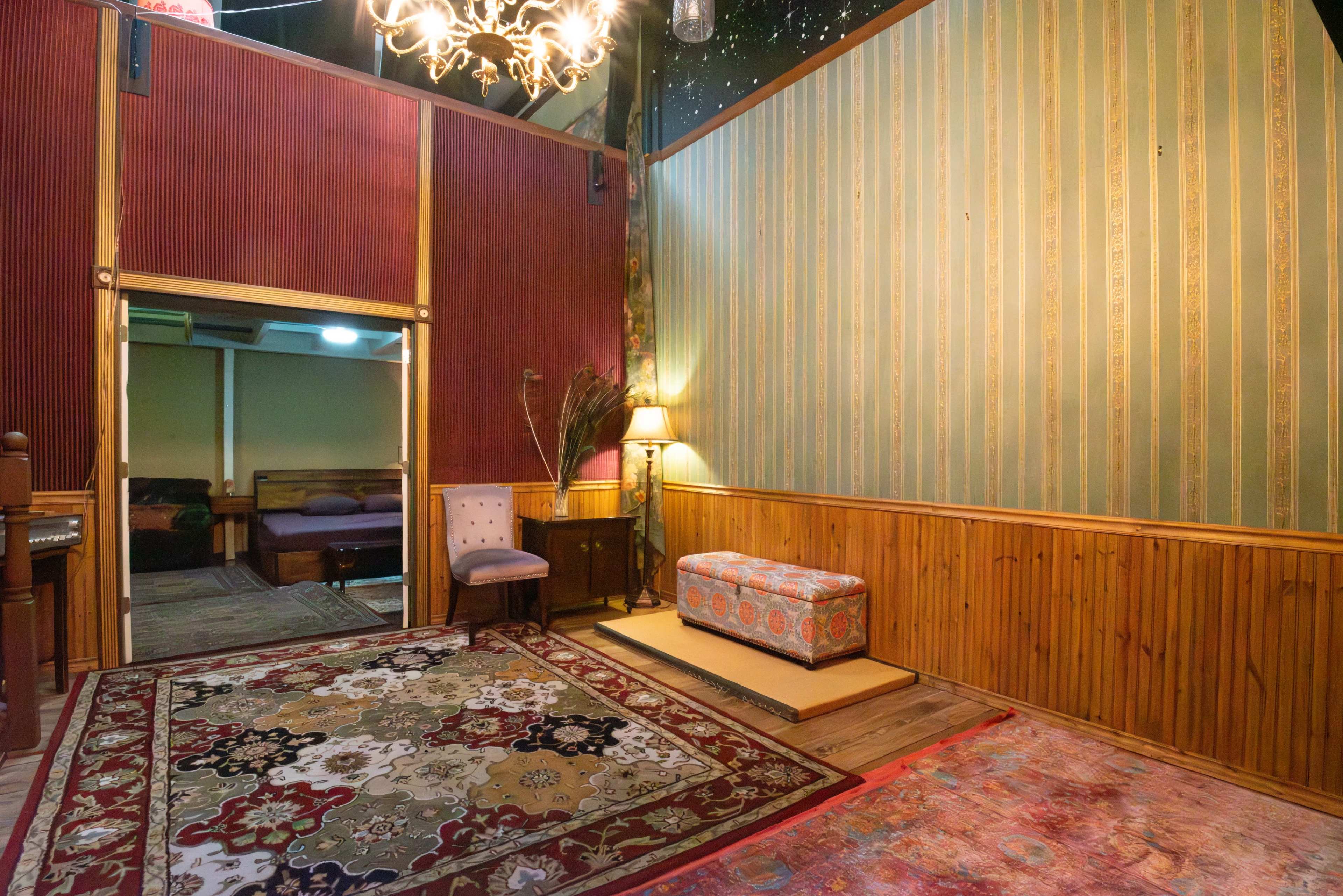 A cozy interior space featuring decorative wallpaper, a patterned rug, and a small sofa beside a lamp.