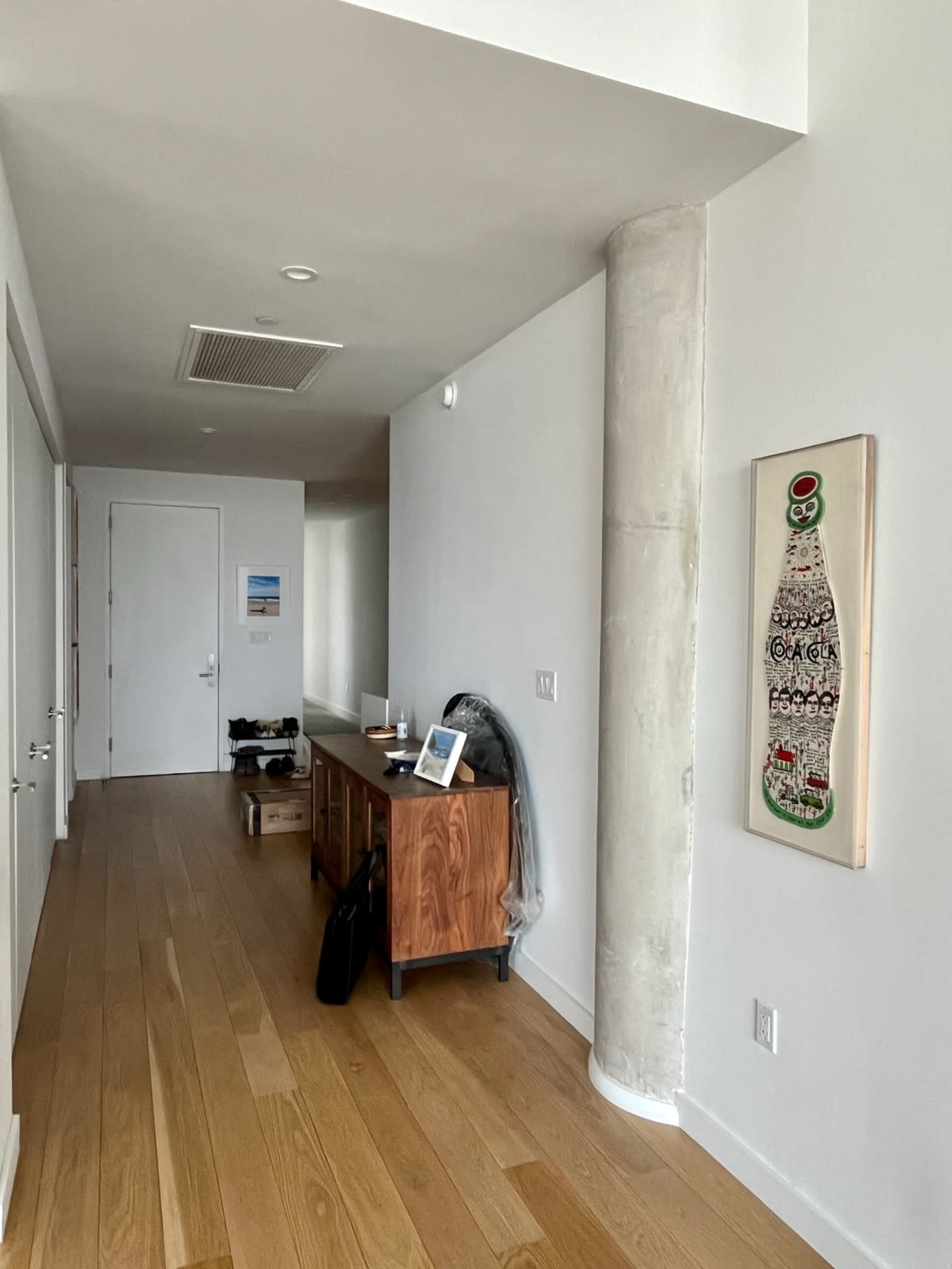 A hallway with a wooden console table, a wall with a decorative piece, and a door at the end of the corridor.