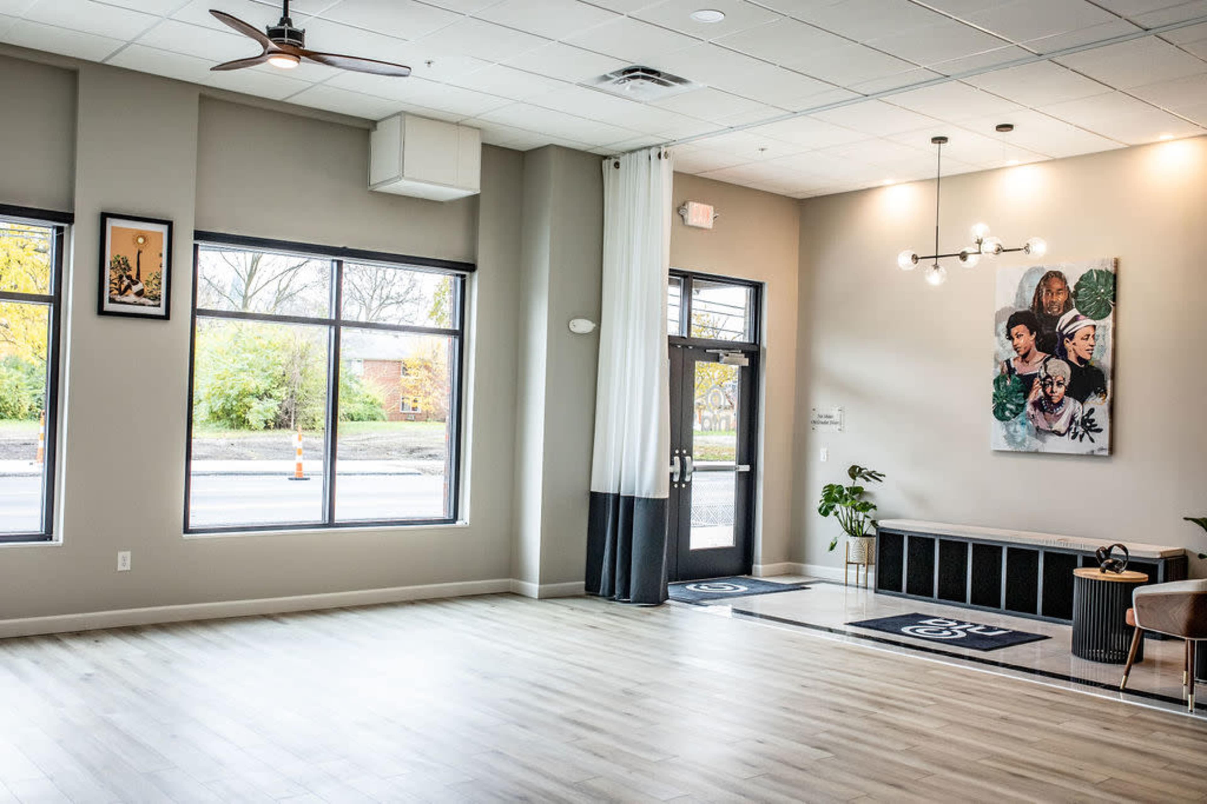 The image depicts a modern, well-lit interior space featuring large windows, minimalist decor, and a mural on the wall.