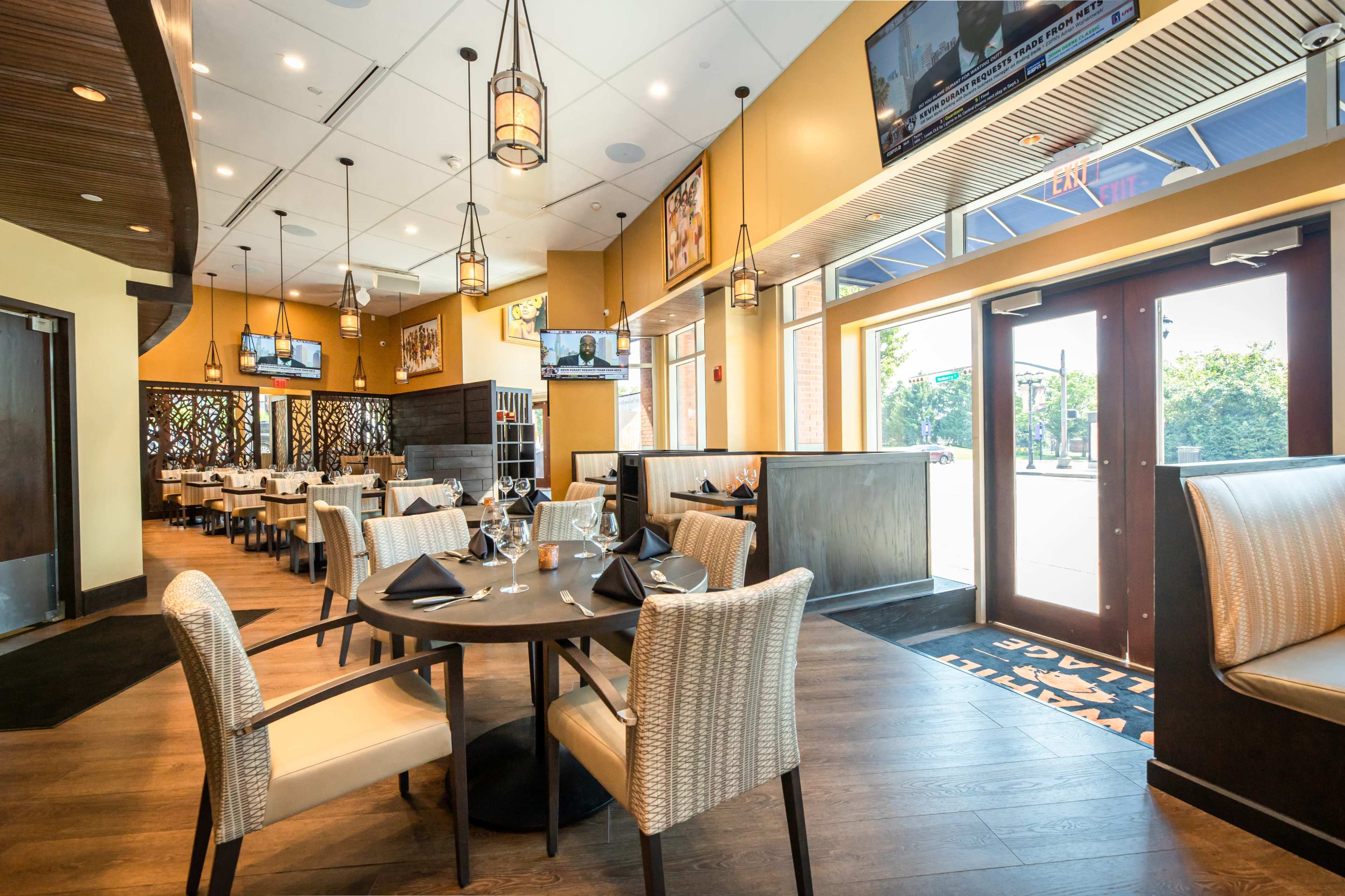 A modern restaurant interior with neatly set tables, chairs, and large windows providing natural light.