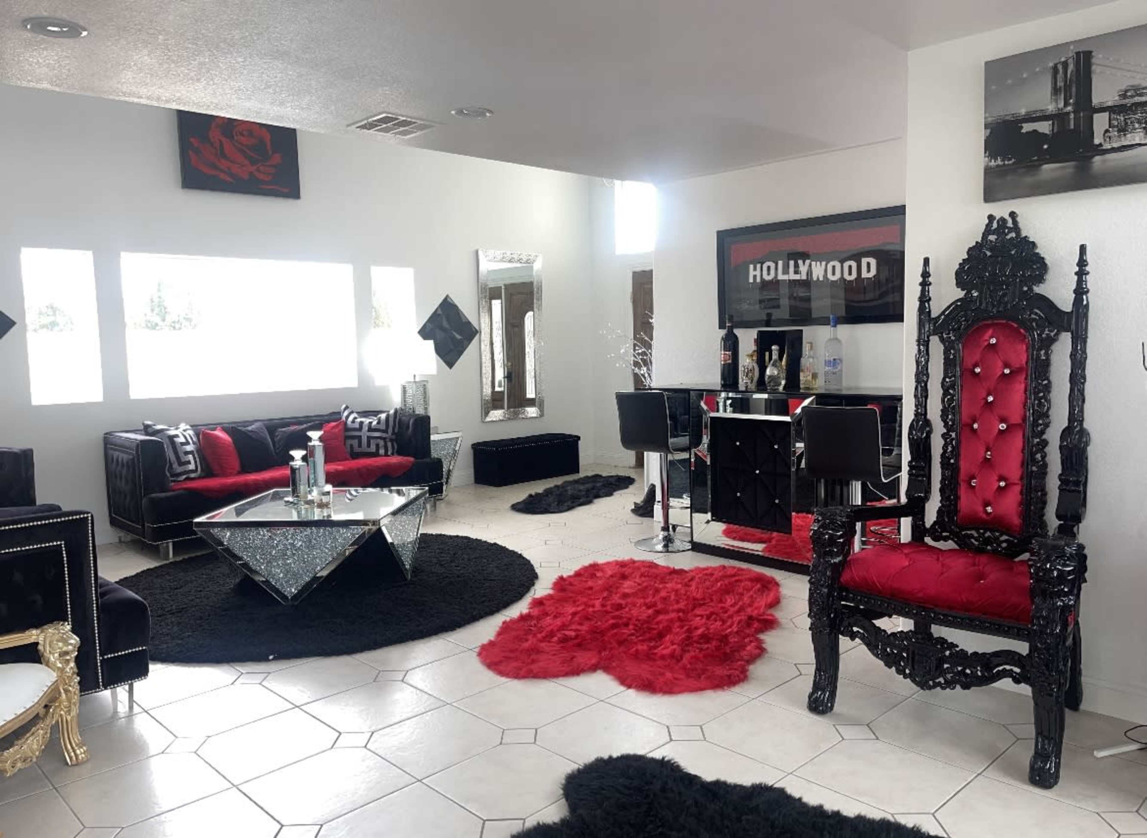 The room features modern furnishings with a black and red color scheme, including a large ornate chair, a glass coffee table, and a bar area.