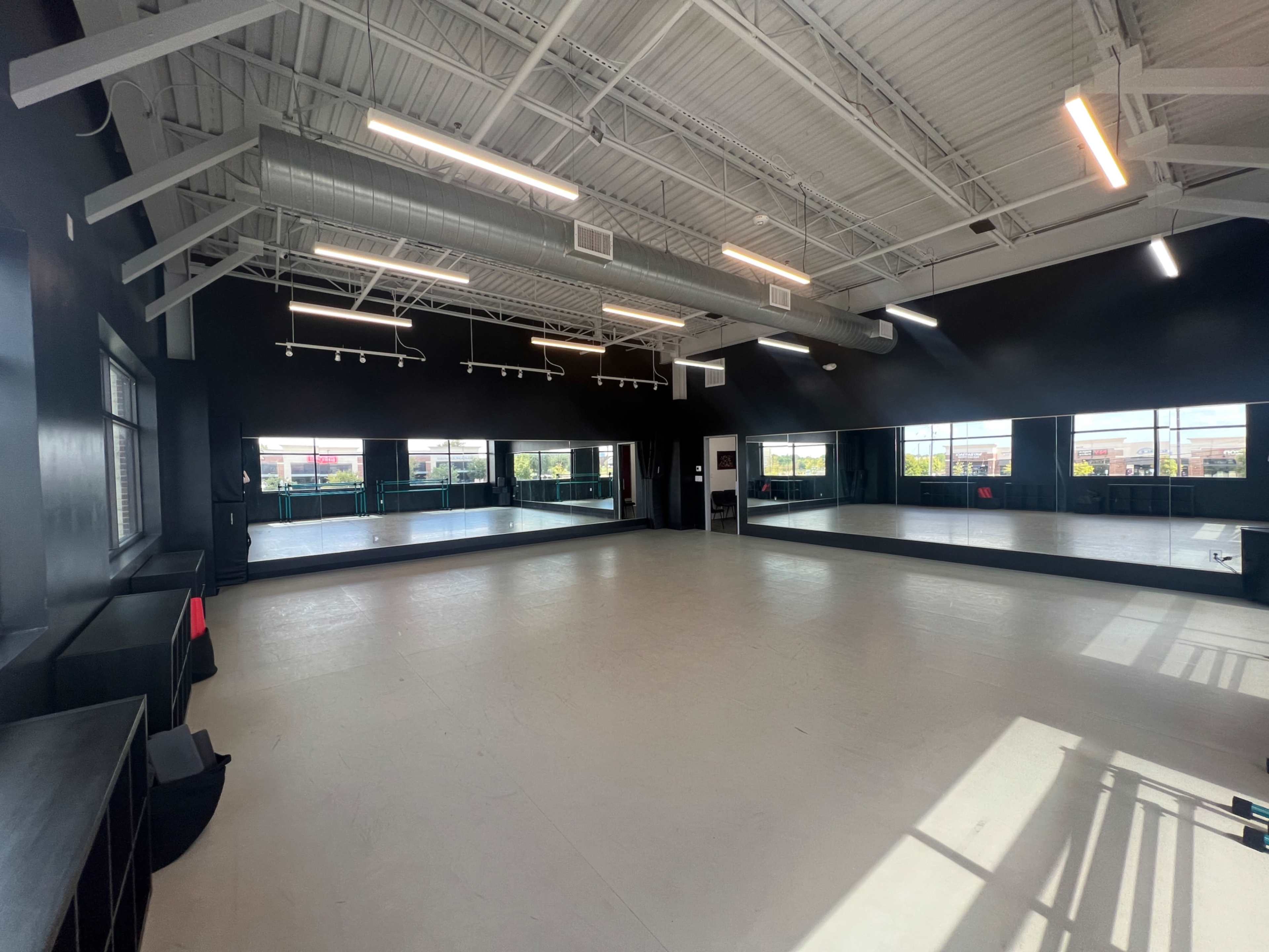 The image shows an empty dance studio with black walls, wooden ceilings, and large mirrors along one side.