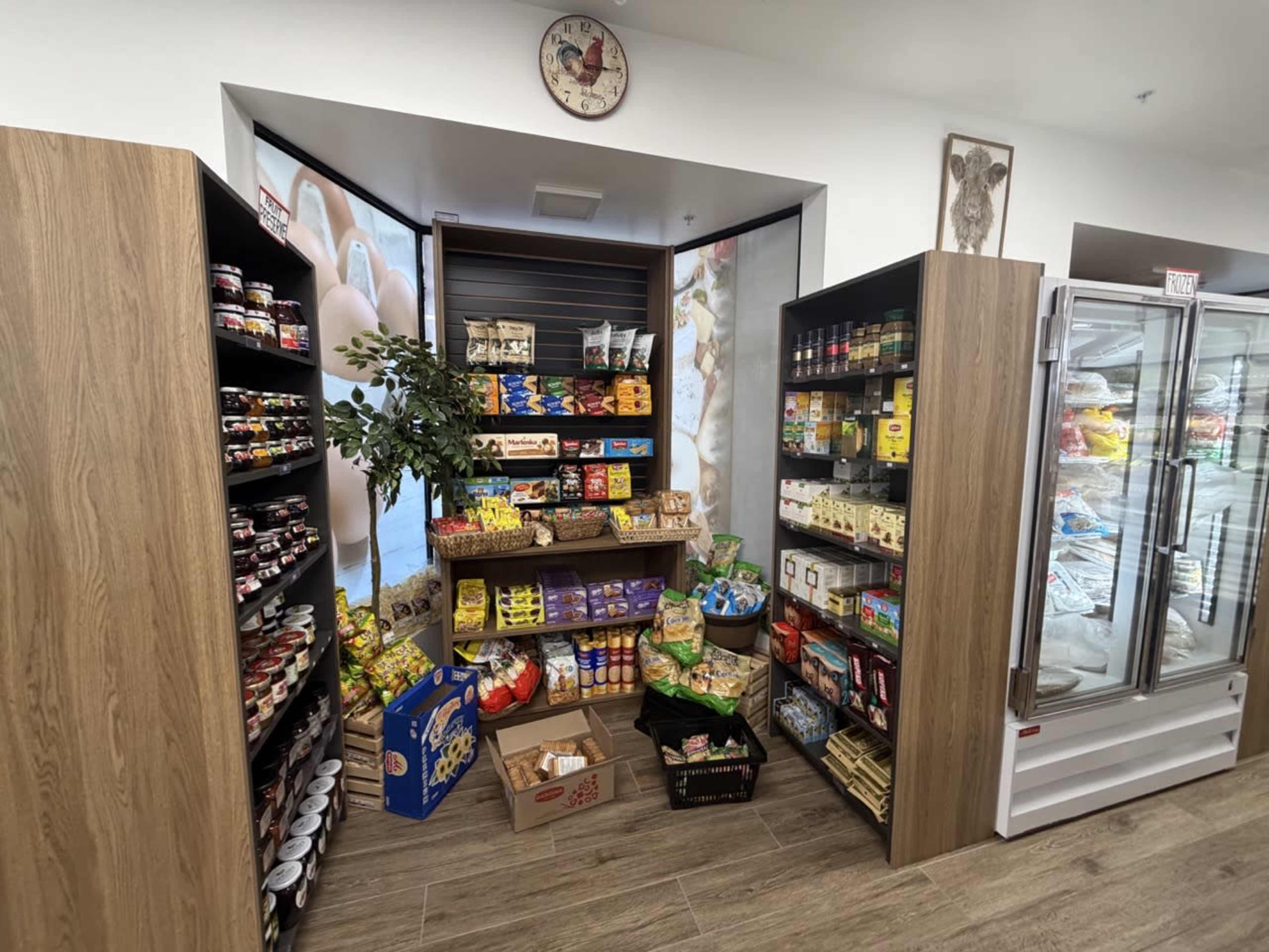 The image shows a small grocery store interior with shelves filled with various packaged food items and a display of snacks in the center.