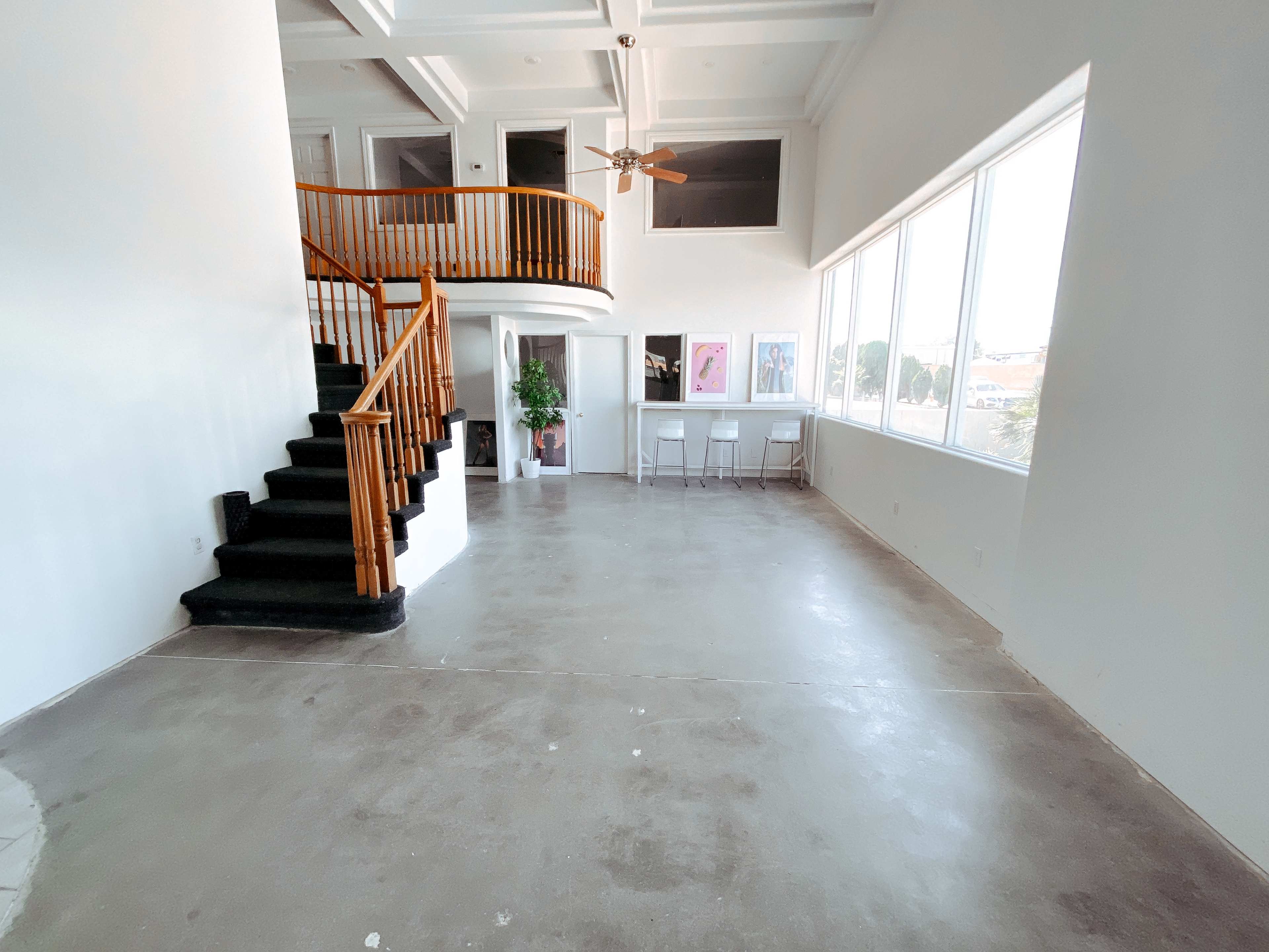 A spacious, empty room featuring a spiral staircase, large windows, and concrete flooring.