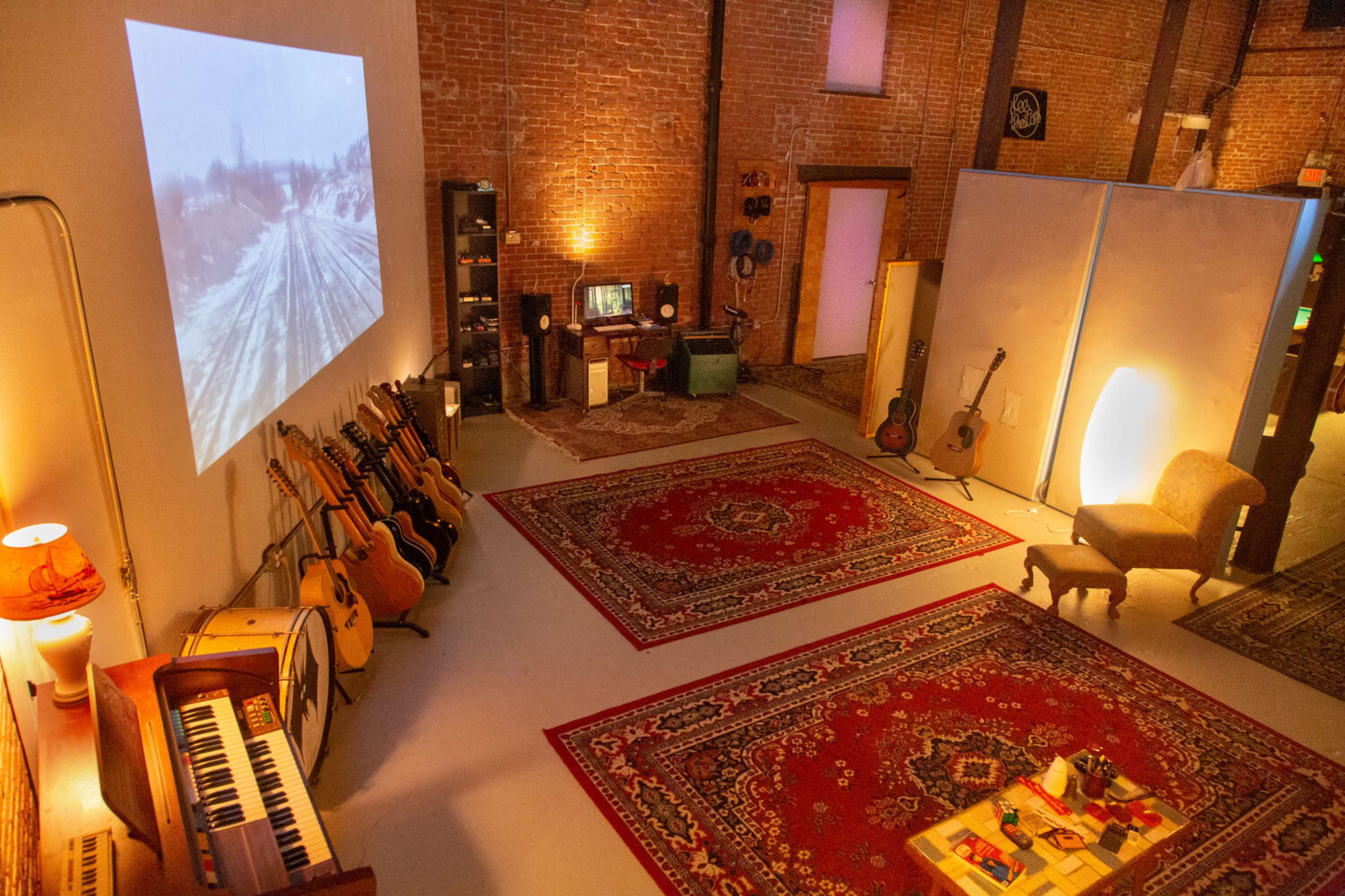 A room with a projection on one wall, various musical instruments arranged on the floor, and a cozy seating area with rugs and furniture.