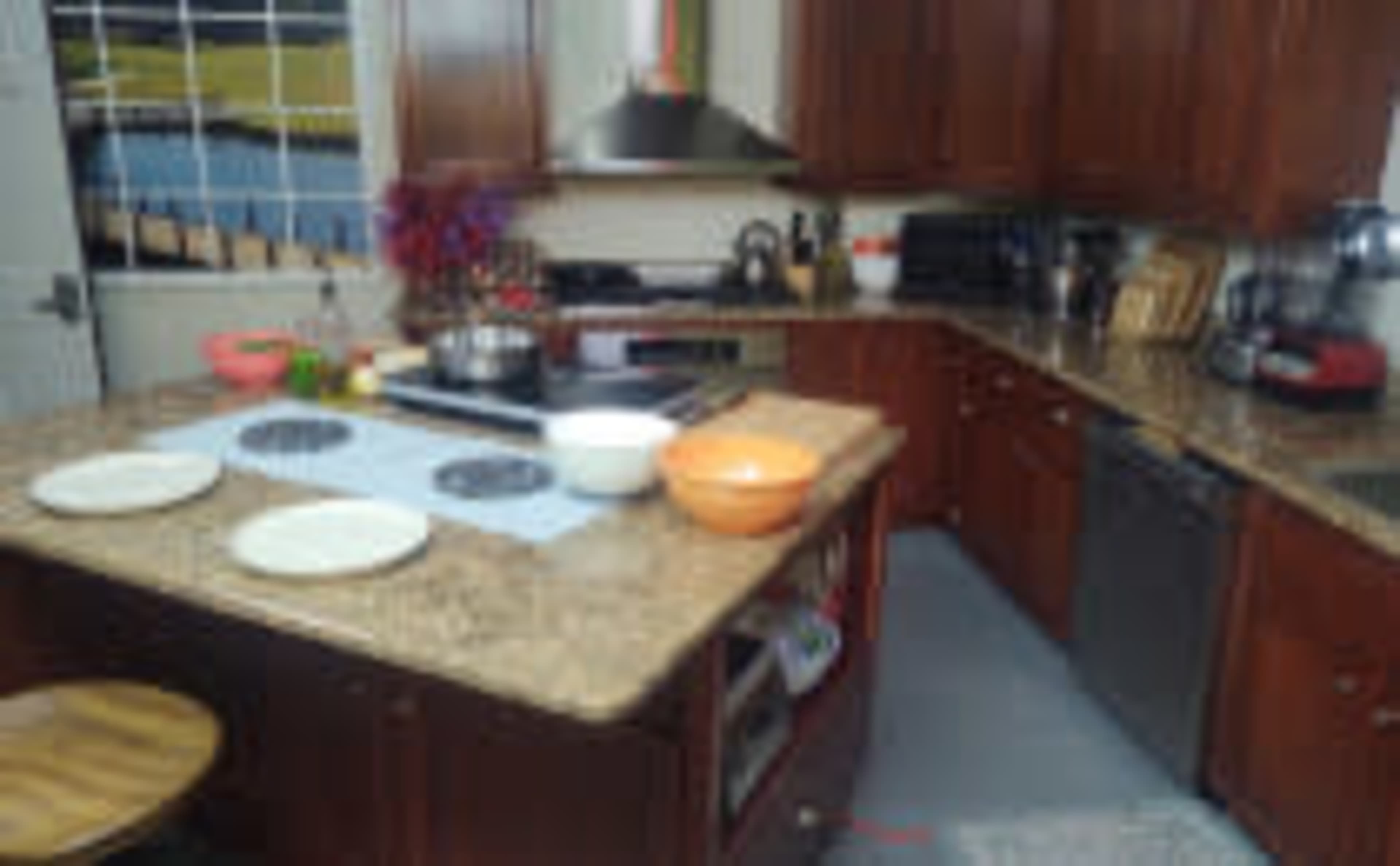 A kitchen features wooden cabinets, a granite countertop with cooking utensils and plates, and an electric stove.