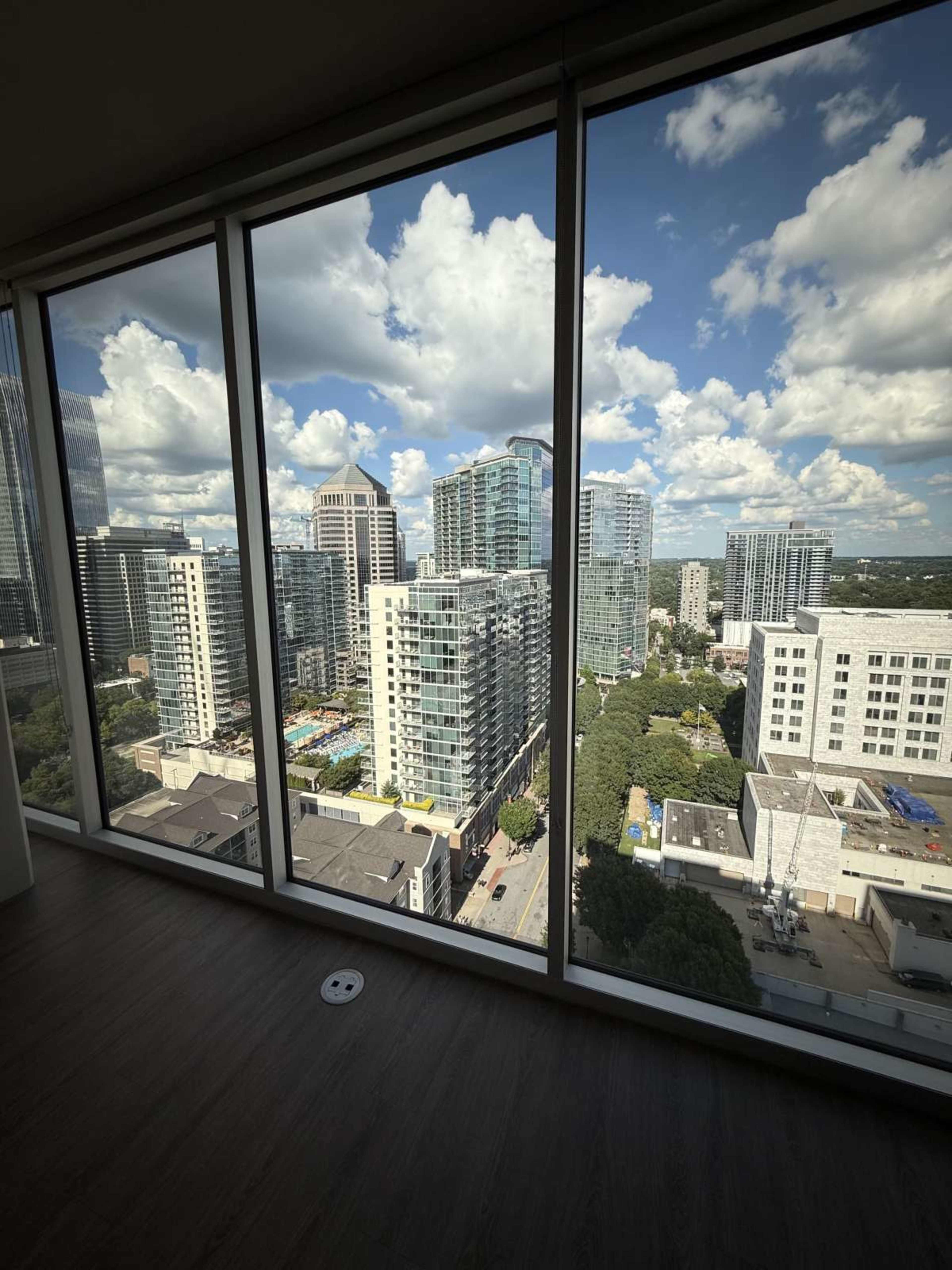 The image shows a city skyline viewed through large glass windows, featuring modern buildings and a clear sky with clouds.
