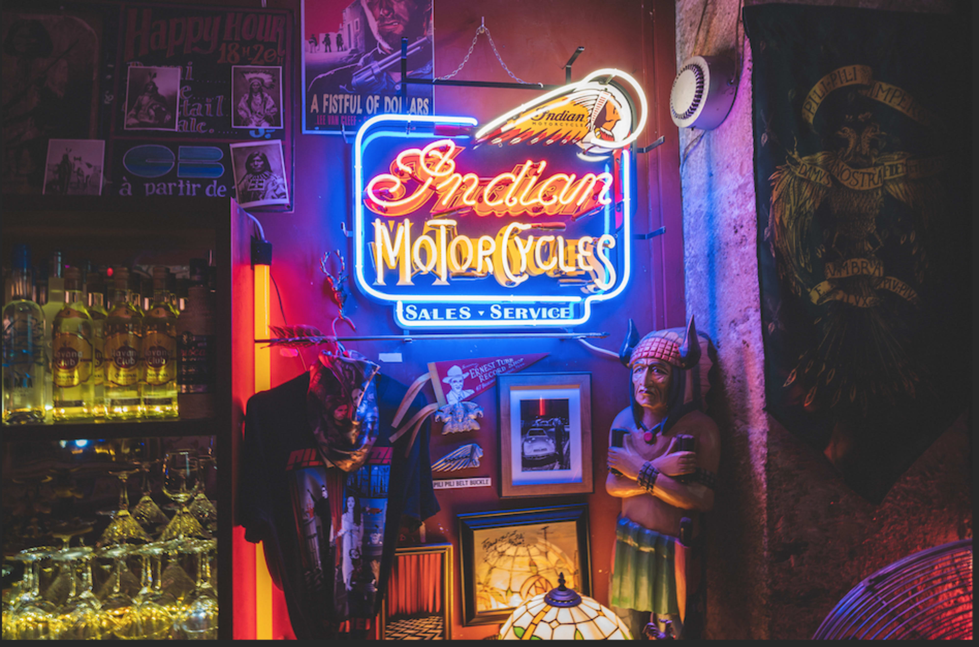 A neon sign for "Indian Motorcycles" illuminated against a backdrop of various collectibles and merchandise, including a statue of a Native American.