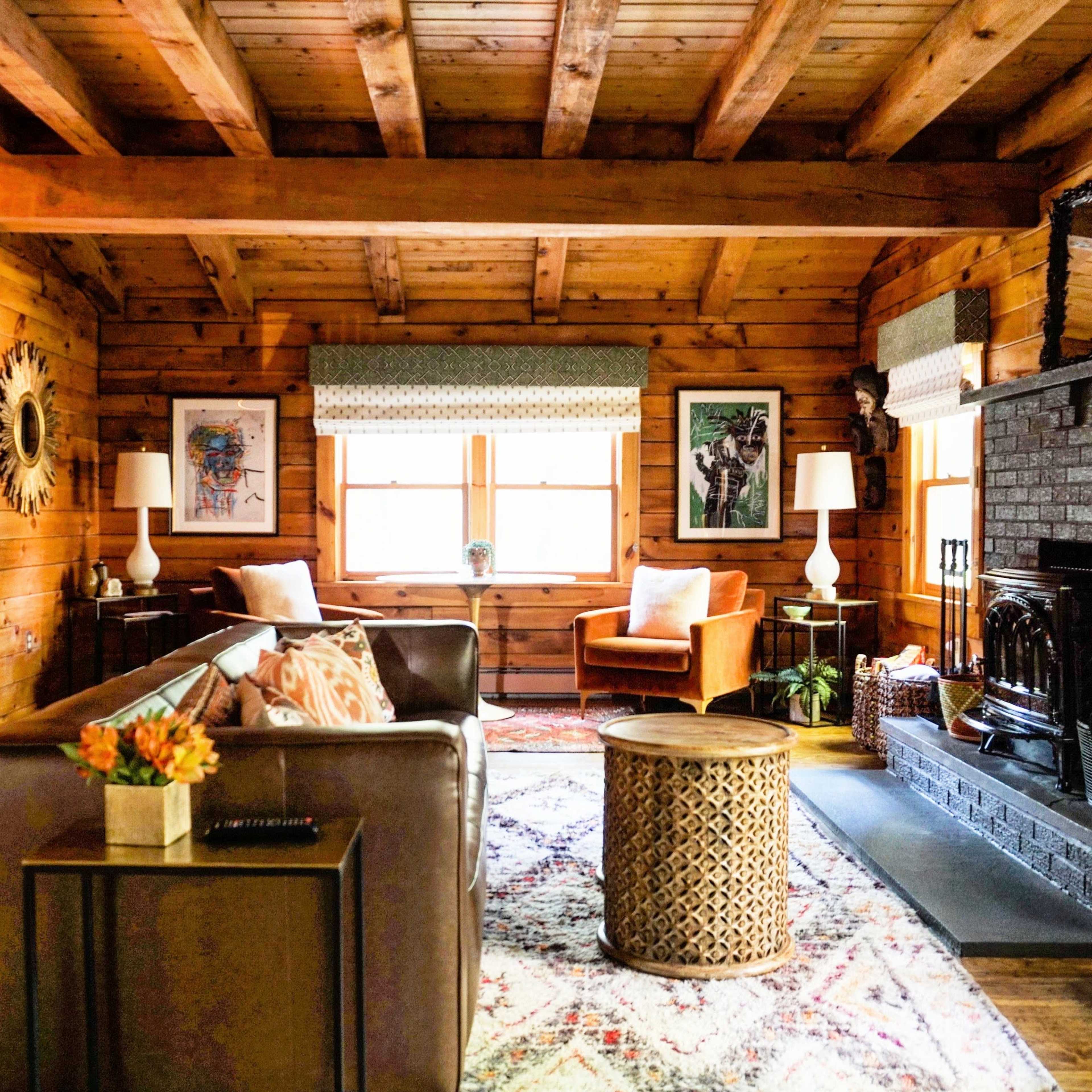A cozy living room with wooden walls, featuring two chairs, a sofa, a circular coffee table, and various pieces of wall art.
