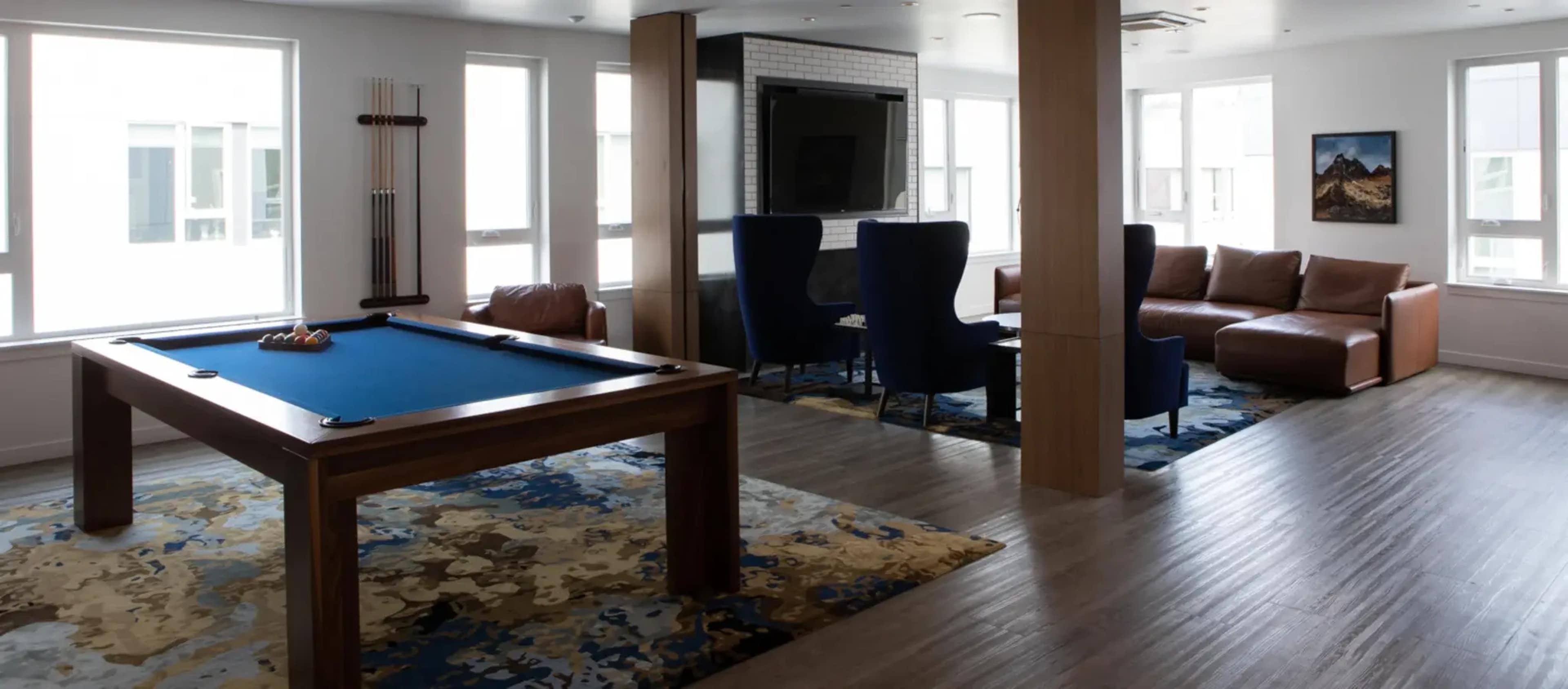 A recreational room featuring a billiards table, seating areas, and large windows.