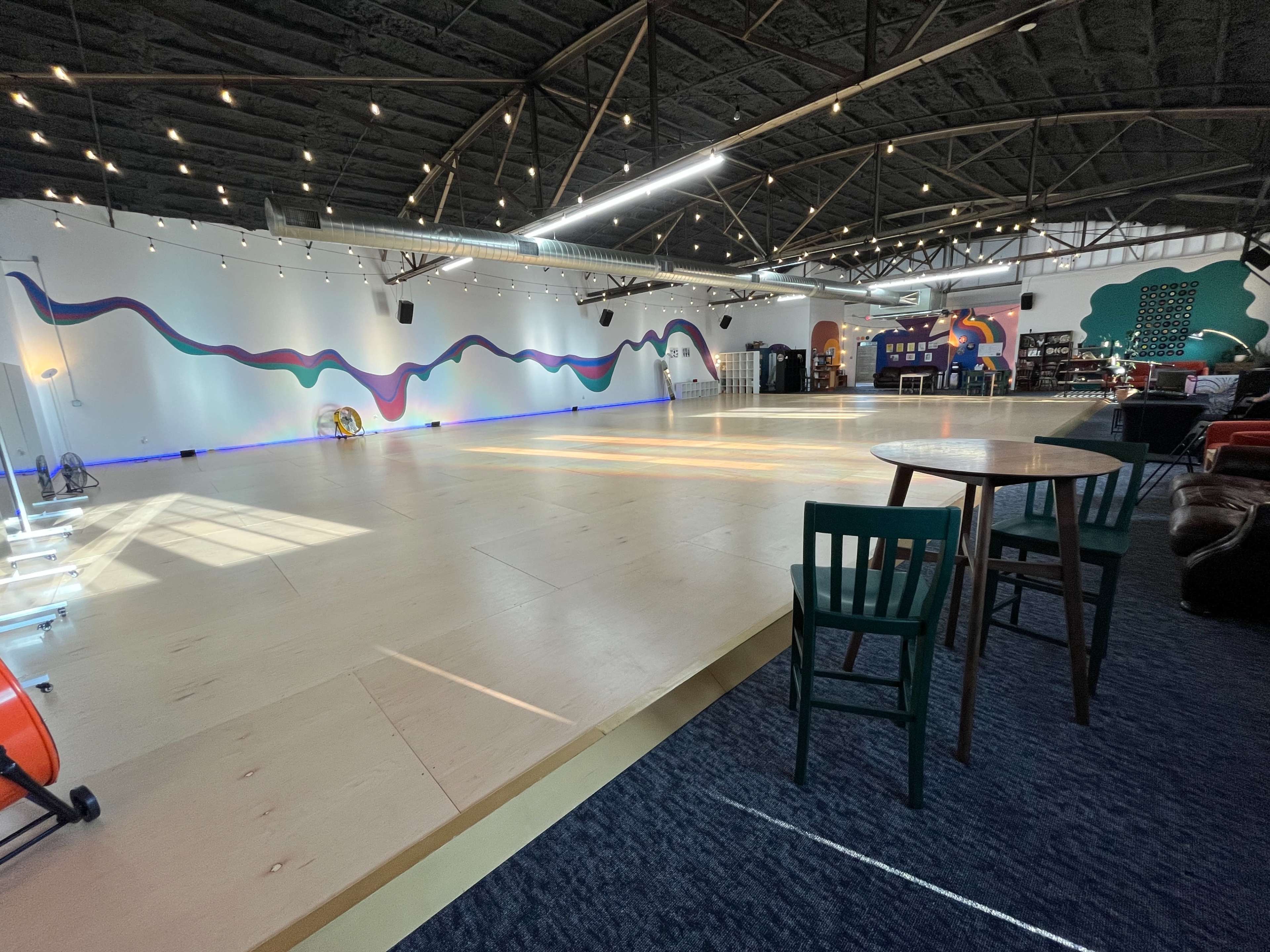 The image shows a spacious, well-lit indoor area with wooden flooring, decorated walls, and various seating arrangements.