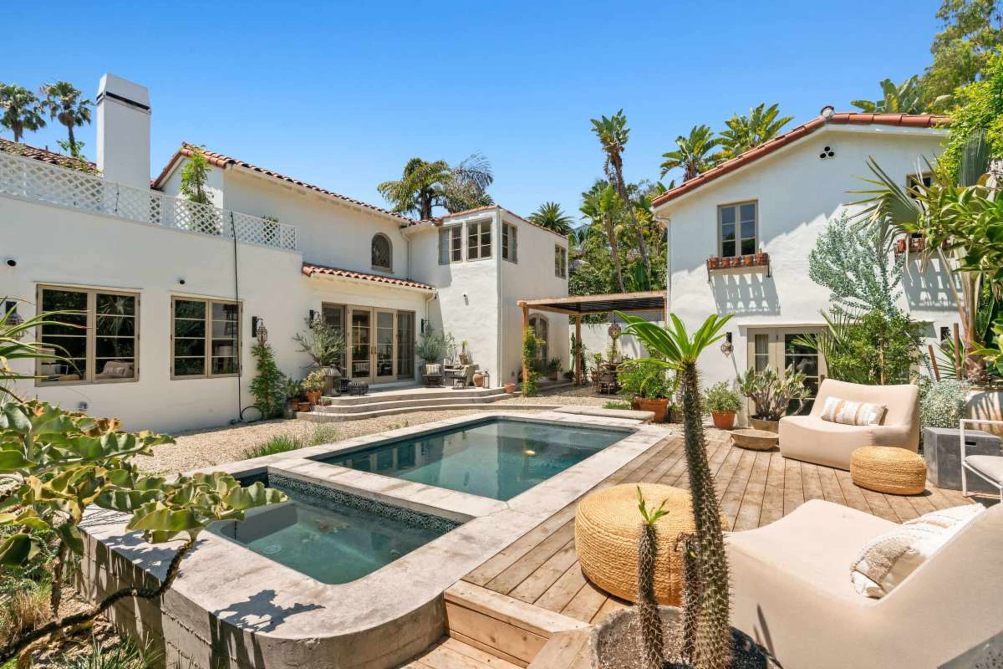 The image shows a spacious outdoor area featuring a pool surrounded by landscaped plants and two white stucco buildings.