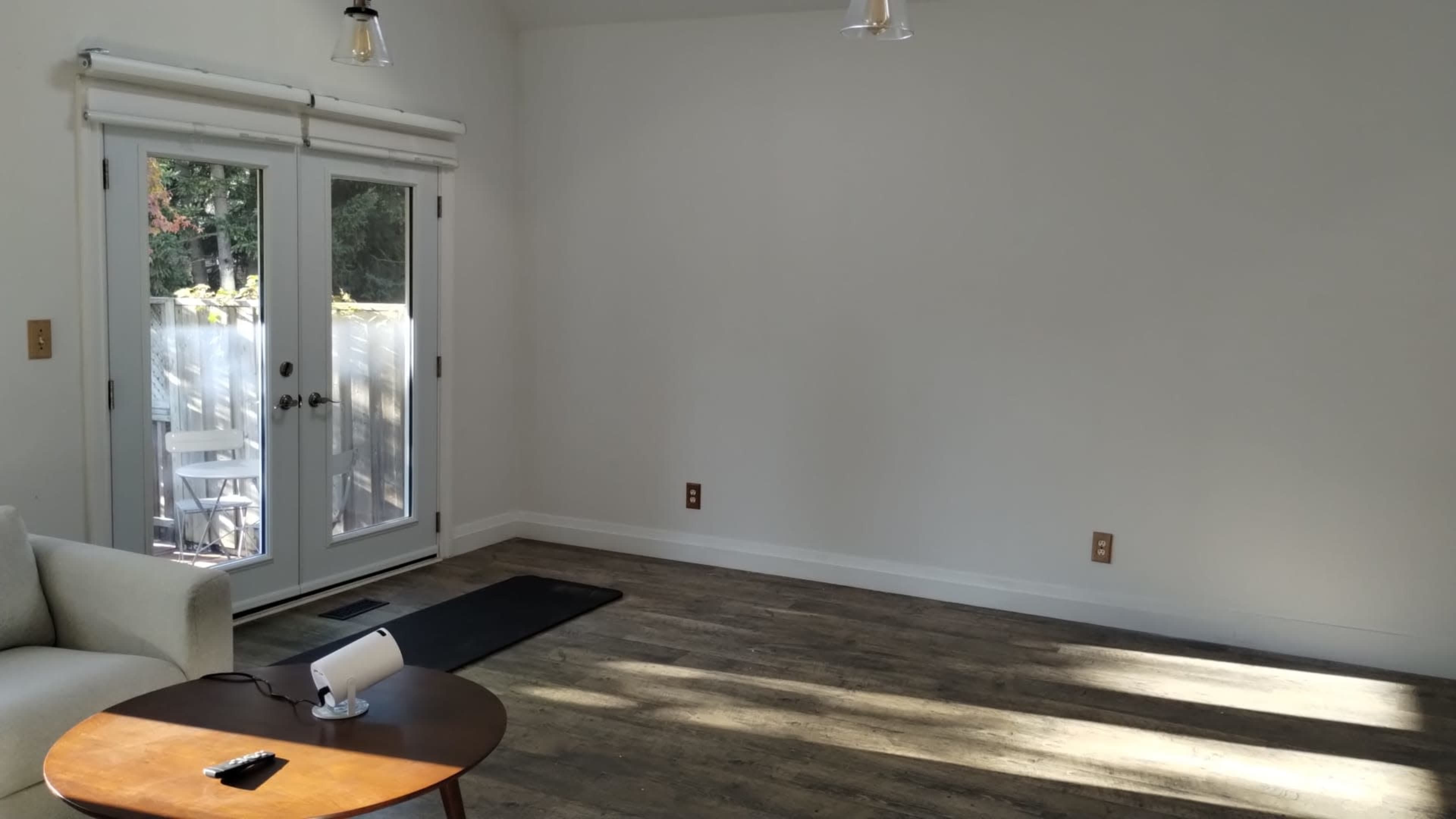 The image shows a well-lit, empty room with a white wall, wooden flooring, and a small table in the foreground.
