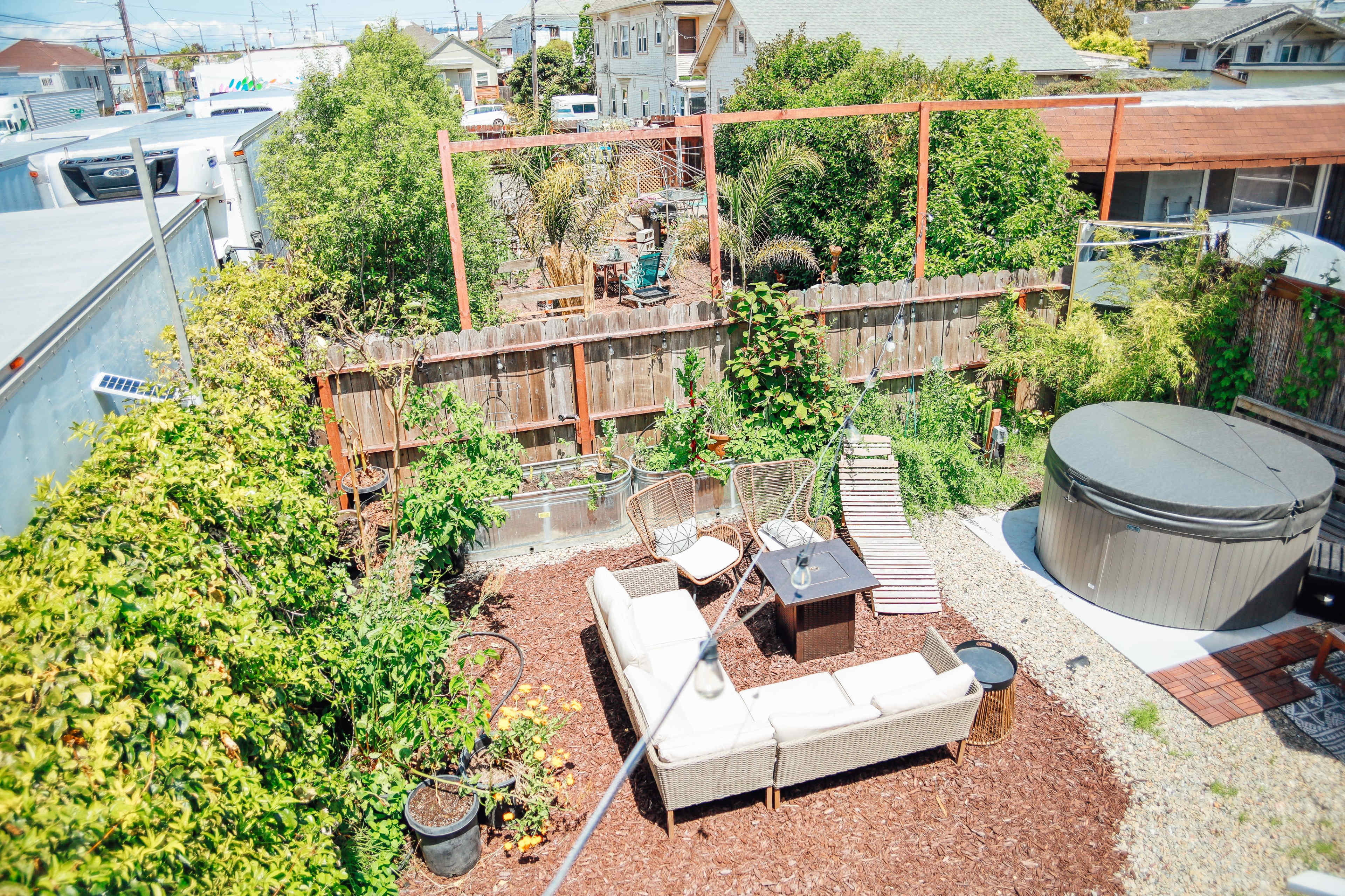 A backyard garden with a seating area, hot tub, and surrounding greenery.