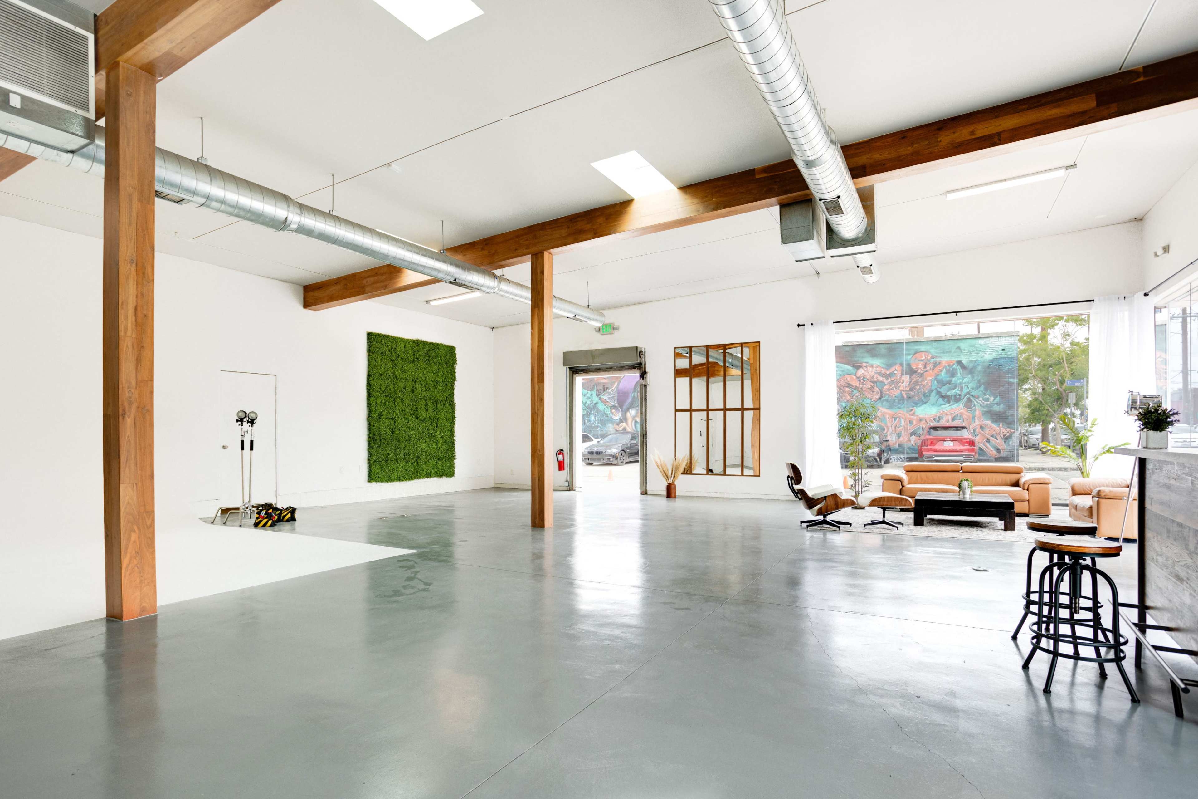 A spacious, minimalist interior with wooden beams, a wall covered in greenery, and a seating area next to large windows featuring a mural outside.