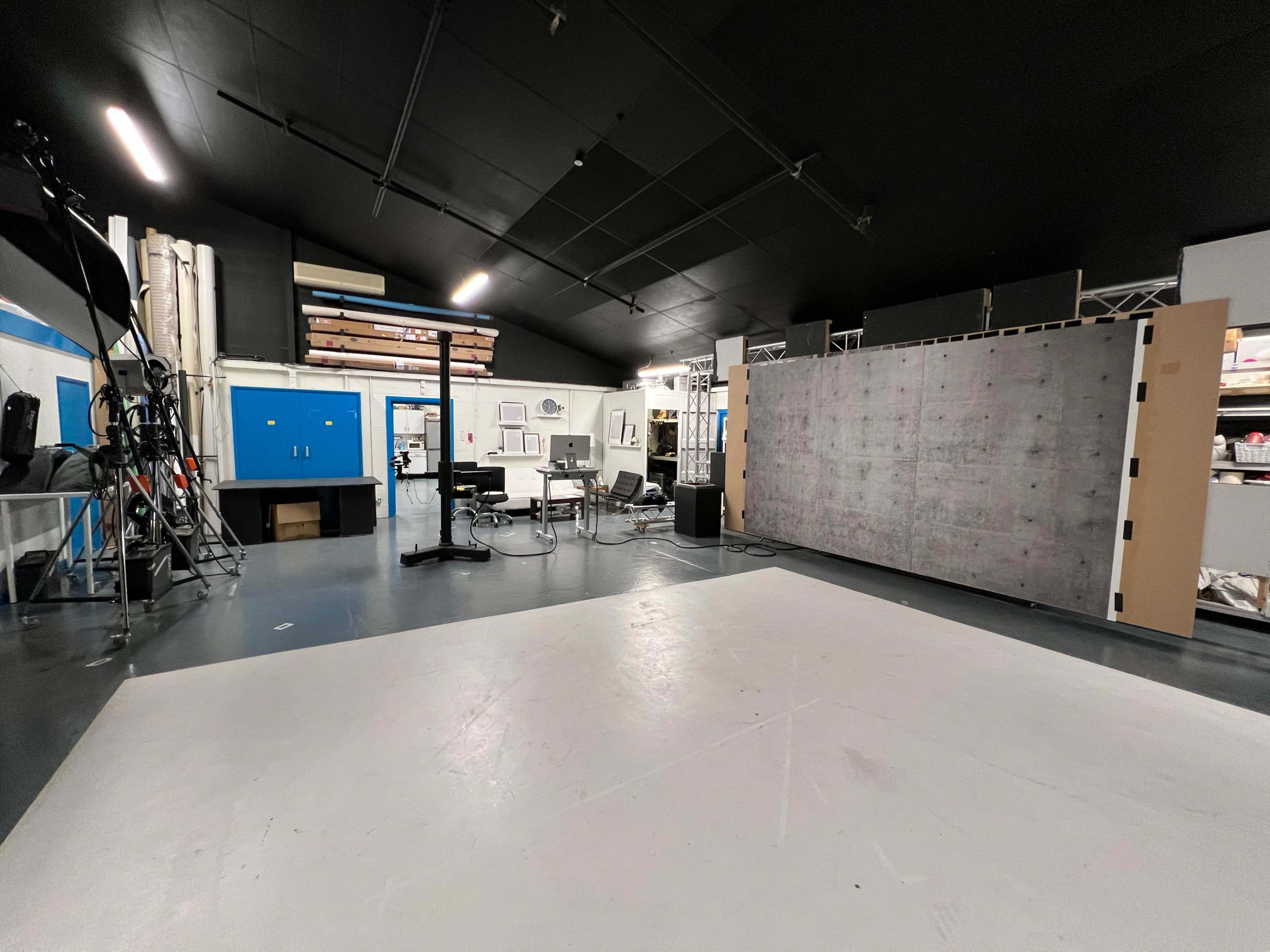 A photography studio with a large, blank backdrop, various equipment, and blue doors in the background.