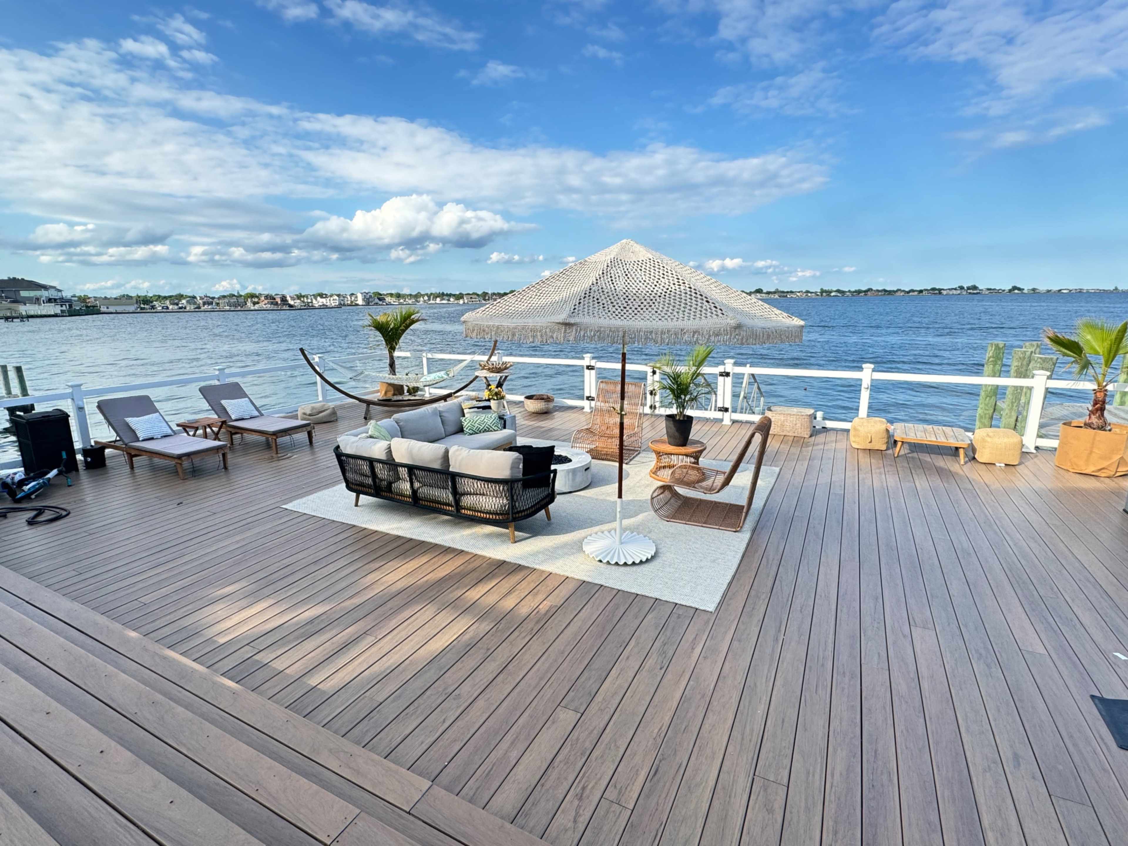 A wooden deck overlooking a body of water, featuring a seating area with furniture and a large umbrella.