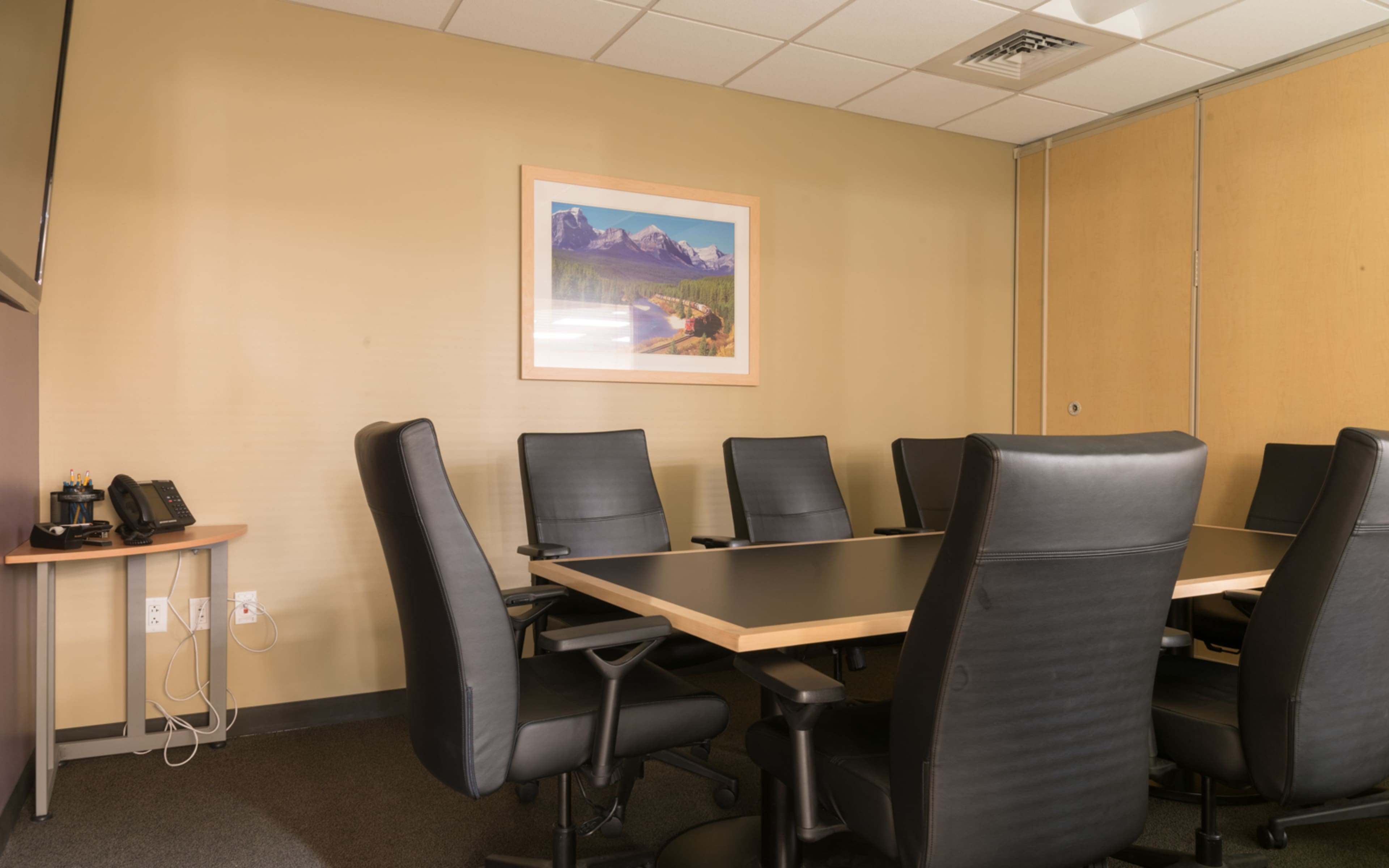A conference room features a large table surrounded by several black leather chairs and a landscape painting on the wall.
