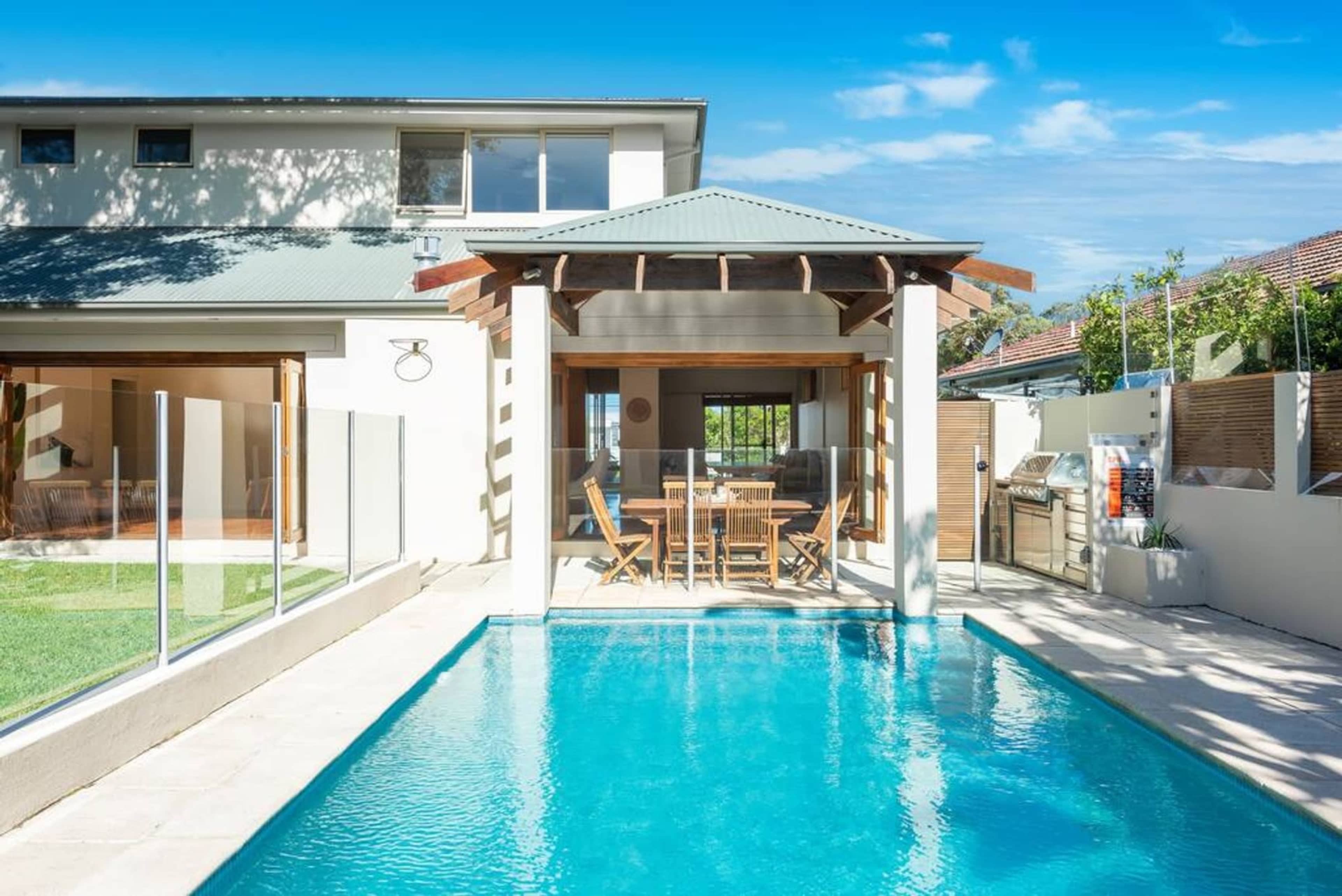 A modern home features a swimming pool beside a spacious patio area with outdoor dining furniture.