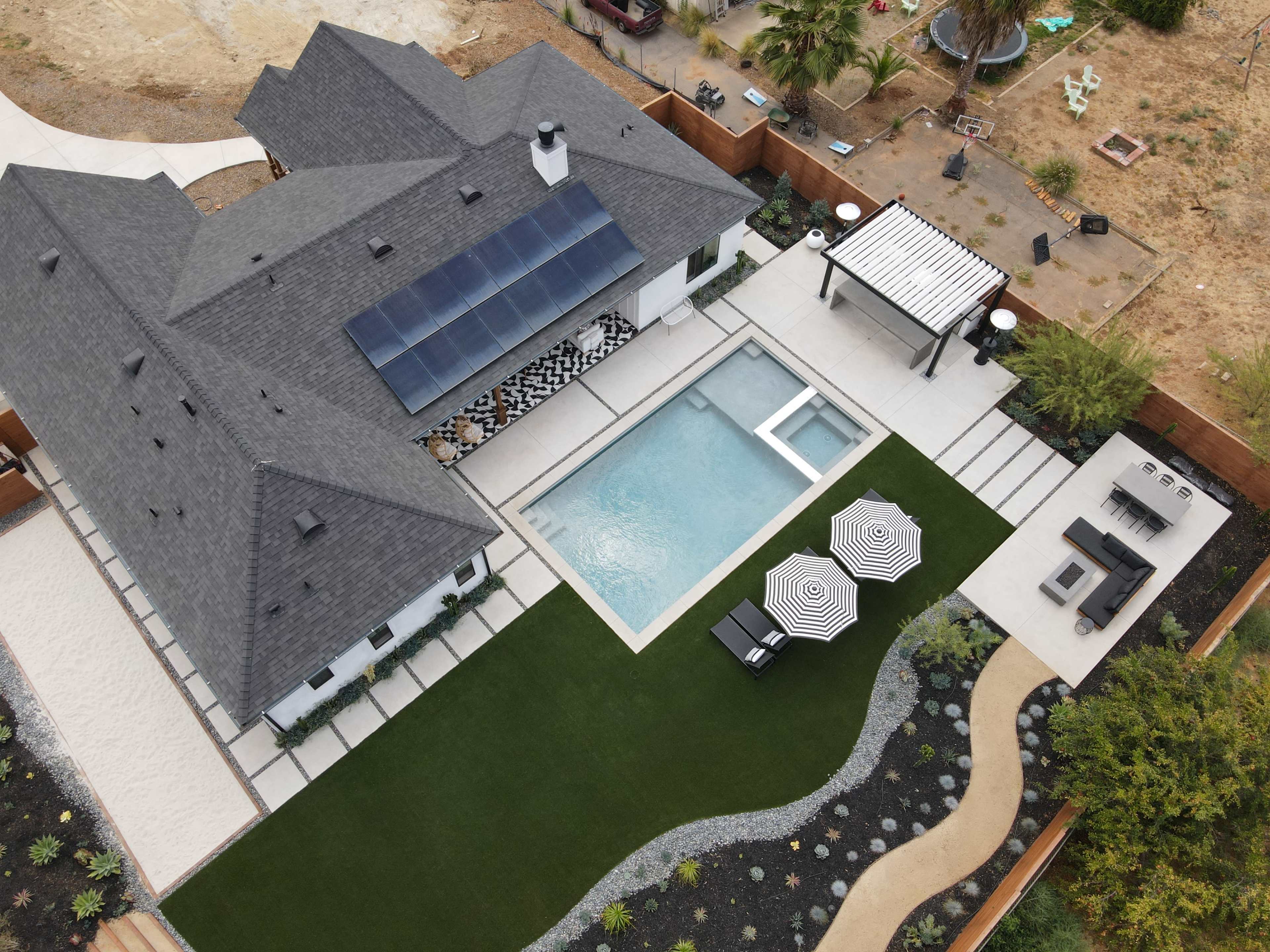A modern house with a swimming pool, a landscaped yard, and outdoor seating areas in a residential neighborhood.