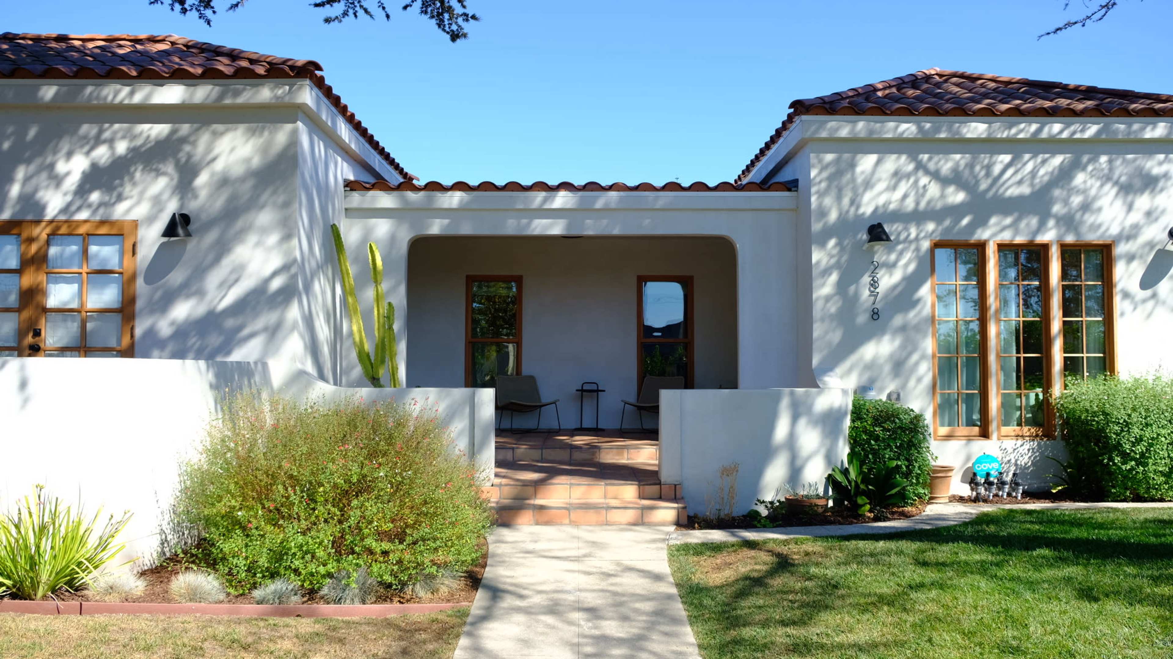 A Spanish-style house with a tiled roof and a walkway leading to a front porch shaded by trees.