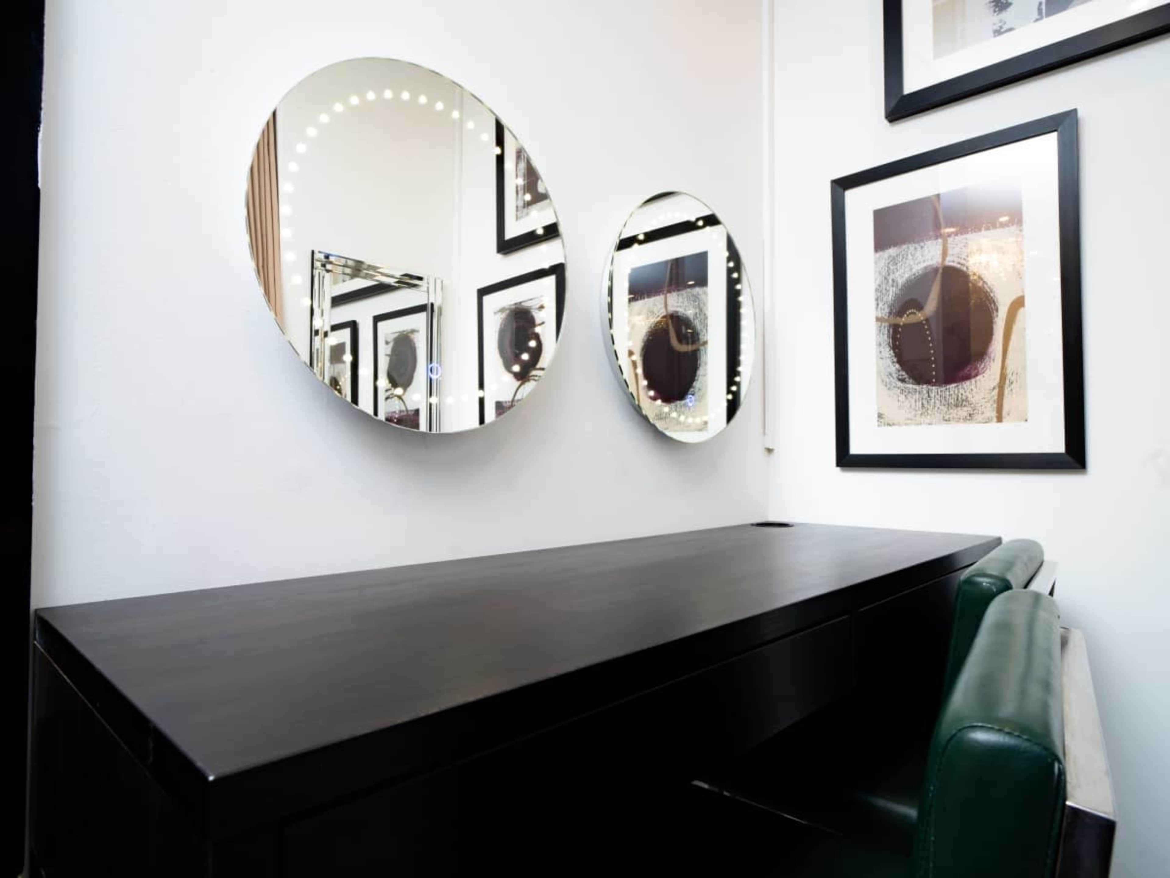 A sleek, dark wooden desk is positioned against a wall featuring three circular mirrors and framed abstract artwork.