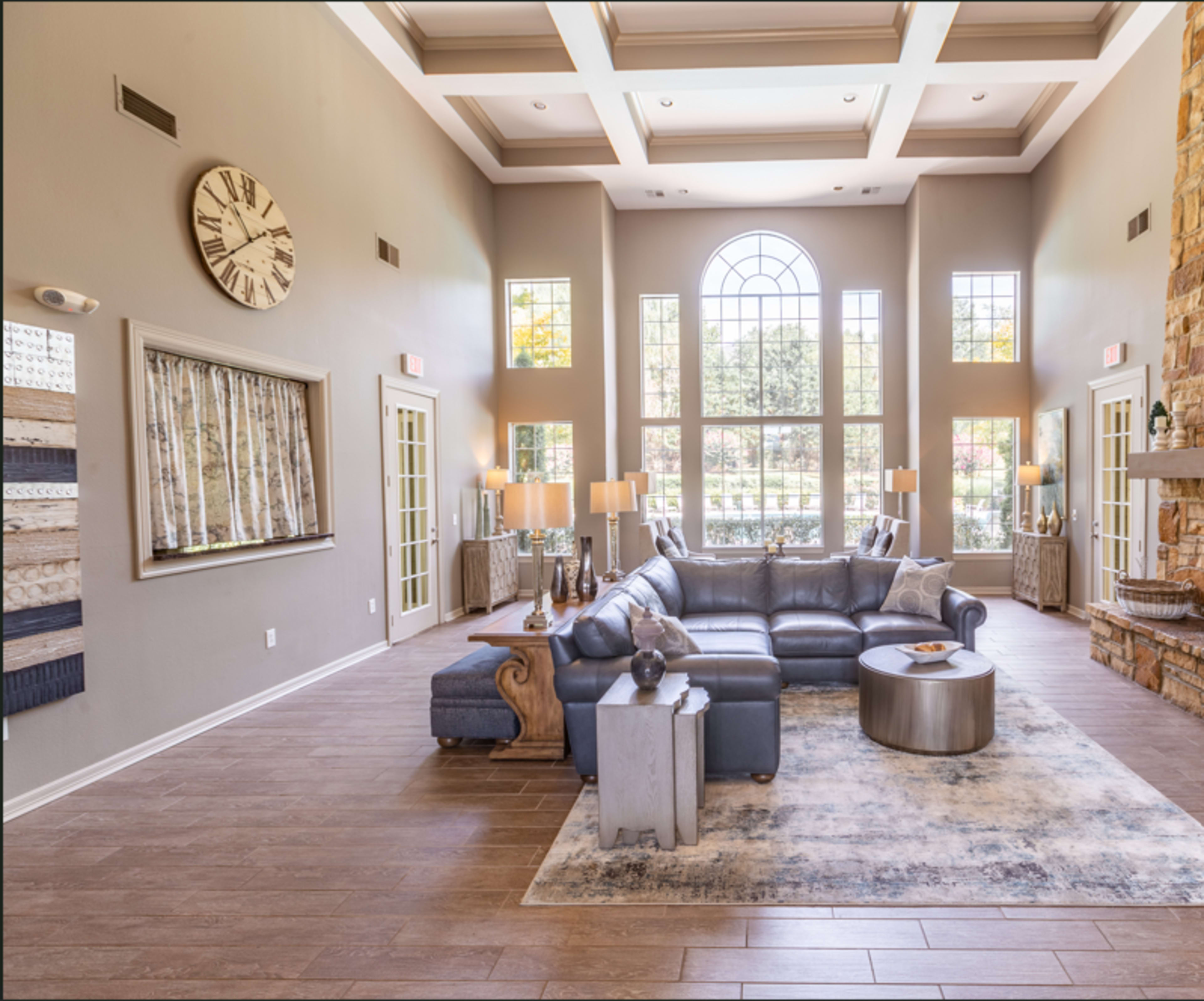 The image shows a spacious living area with a large sectional couch, a round coffee table, and large windows letting in natural light.