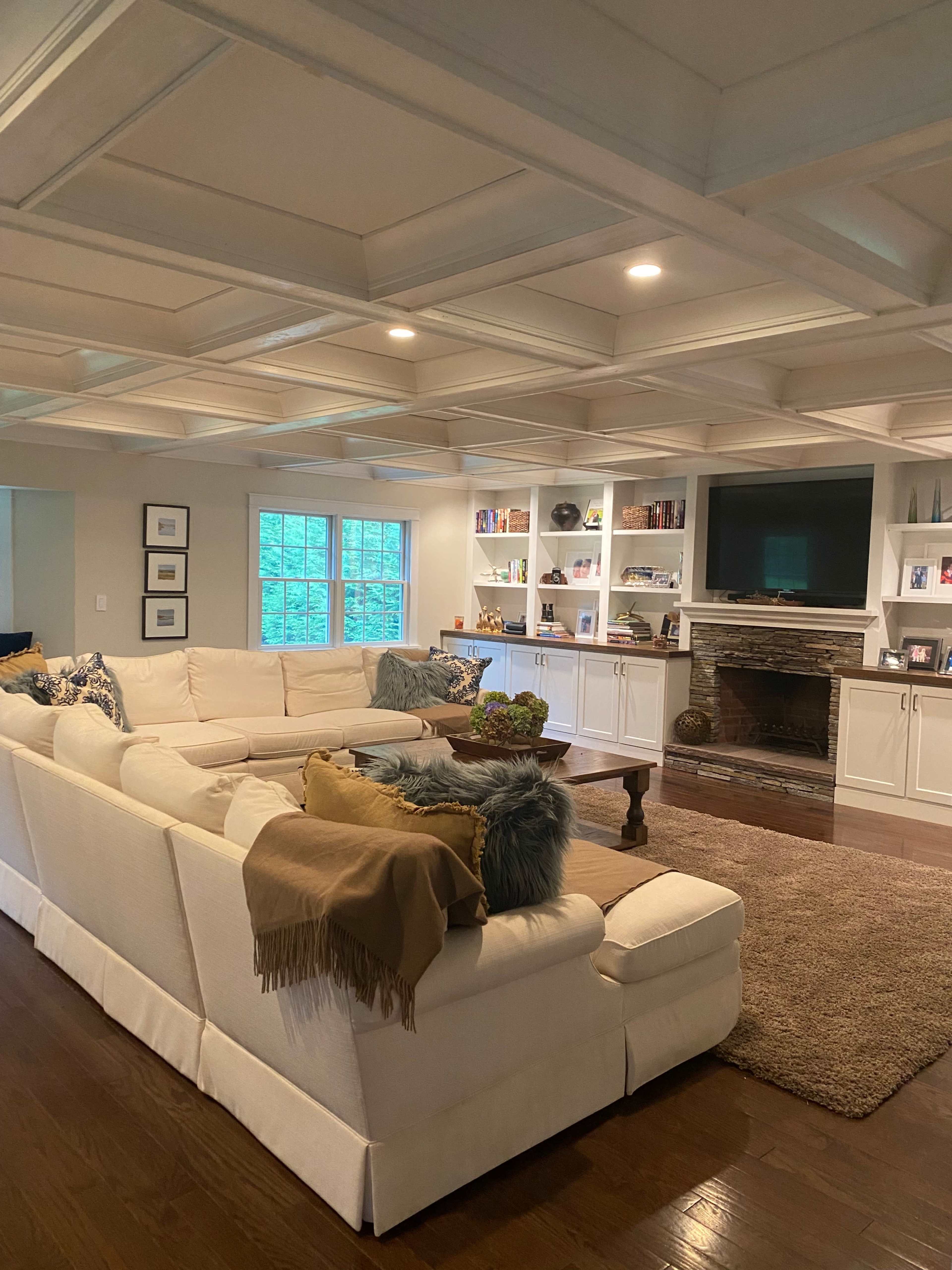 A spacious living room with a large white sectional sofa, a wooden coffee table, and built-in shelves surrounding a stone fireplace.