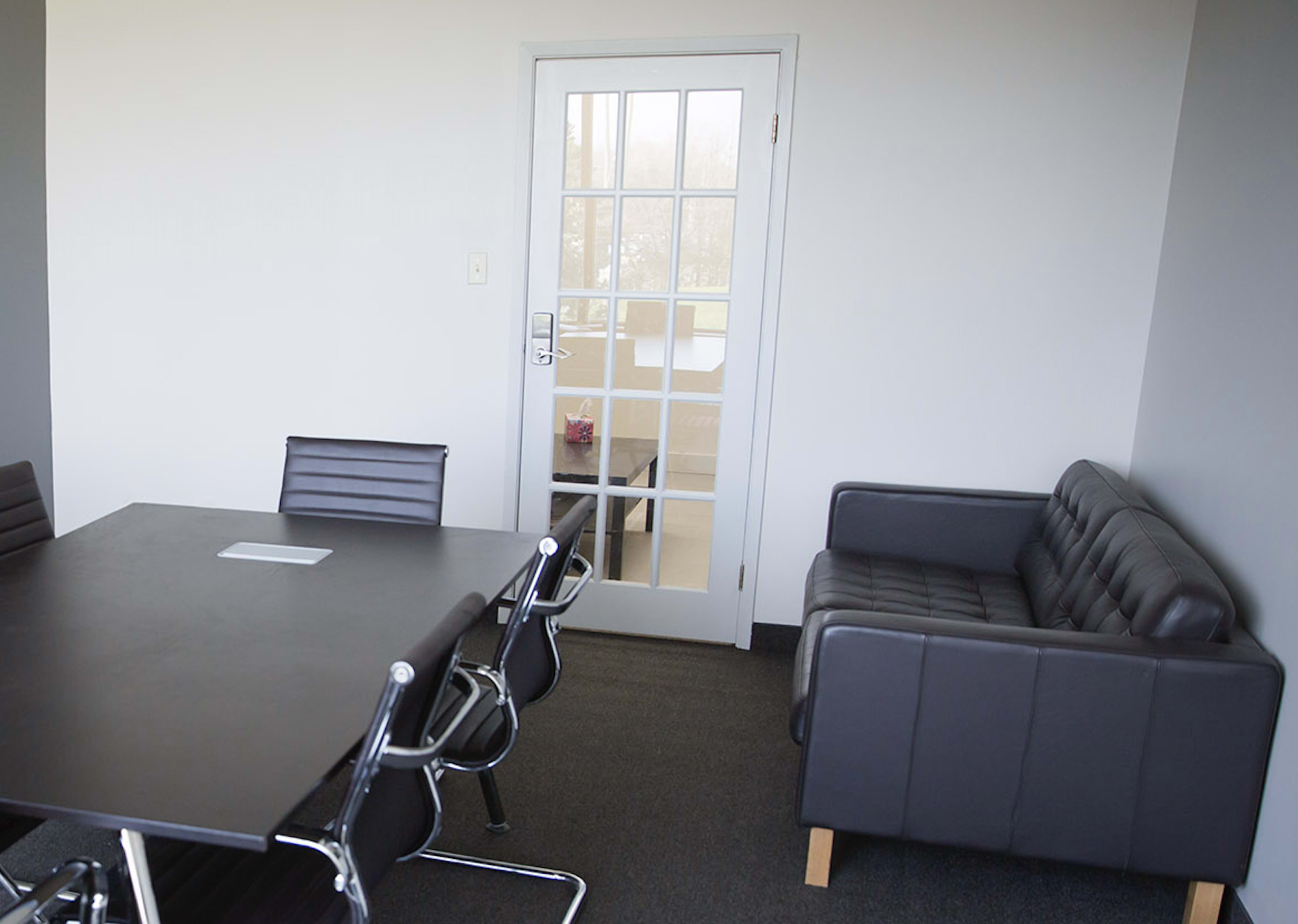 A conference room features a rectangular table with several black chairs and a black couch next to a glass-paneled door.