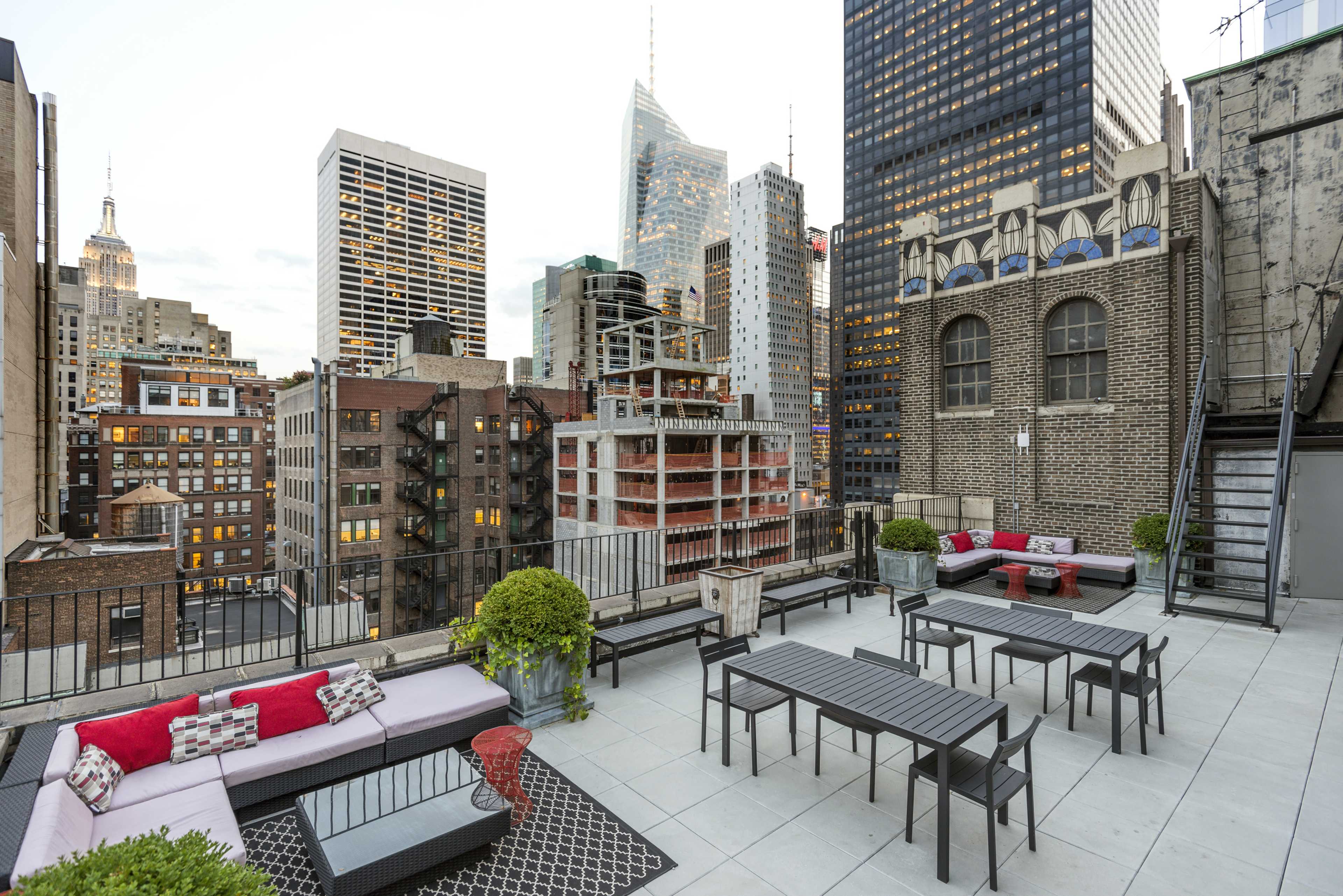 A rooftop terrace with modern furniture, overlooking a city skyline that includes the Empire State Building.