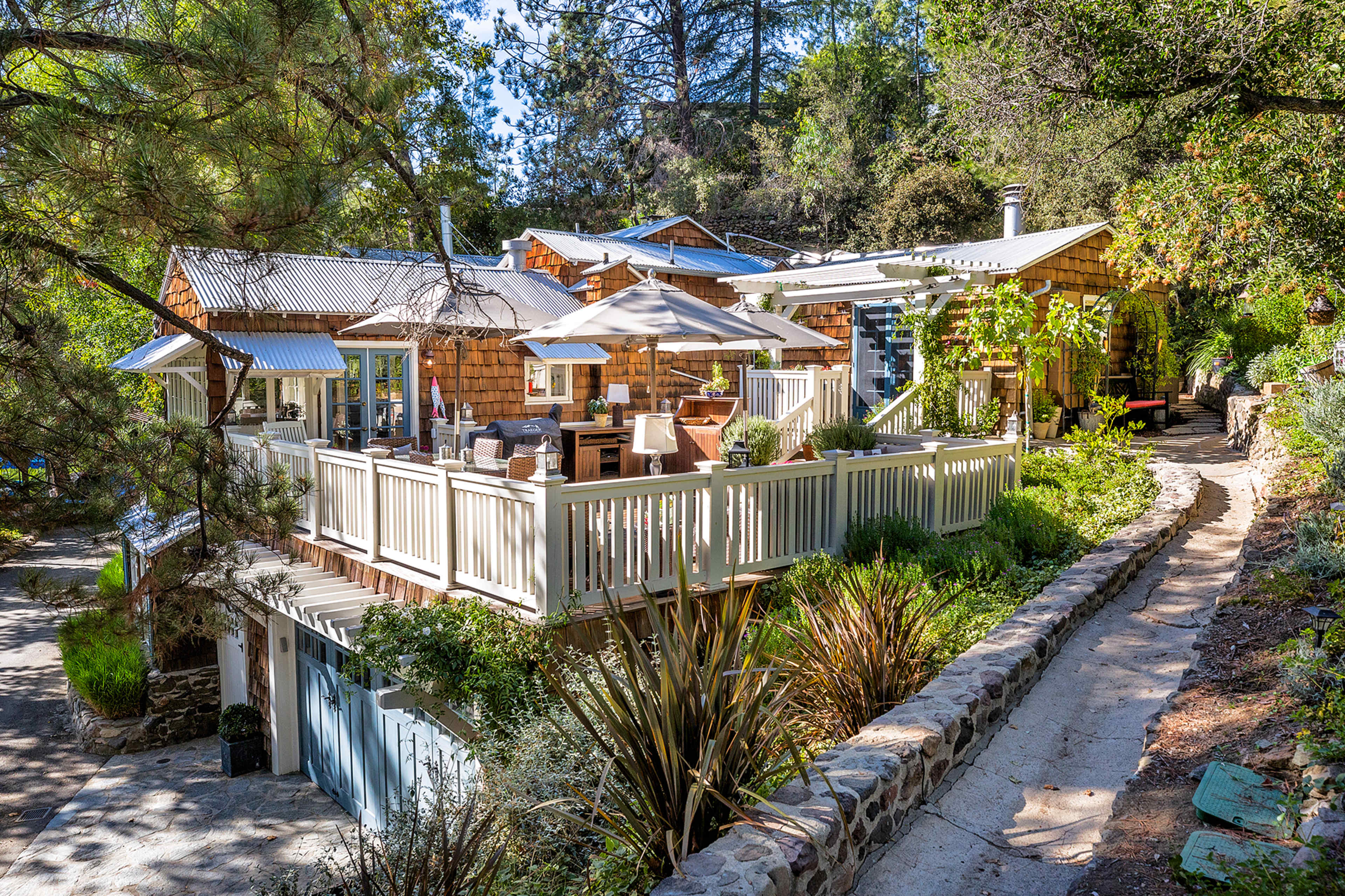 A multi-level house with a wooden exterior surrounded by trees and a winding stone pathway leads to it.