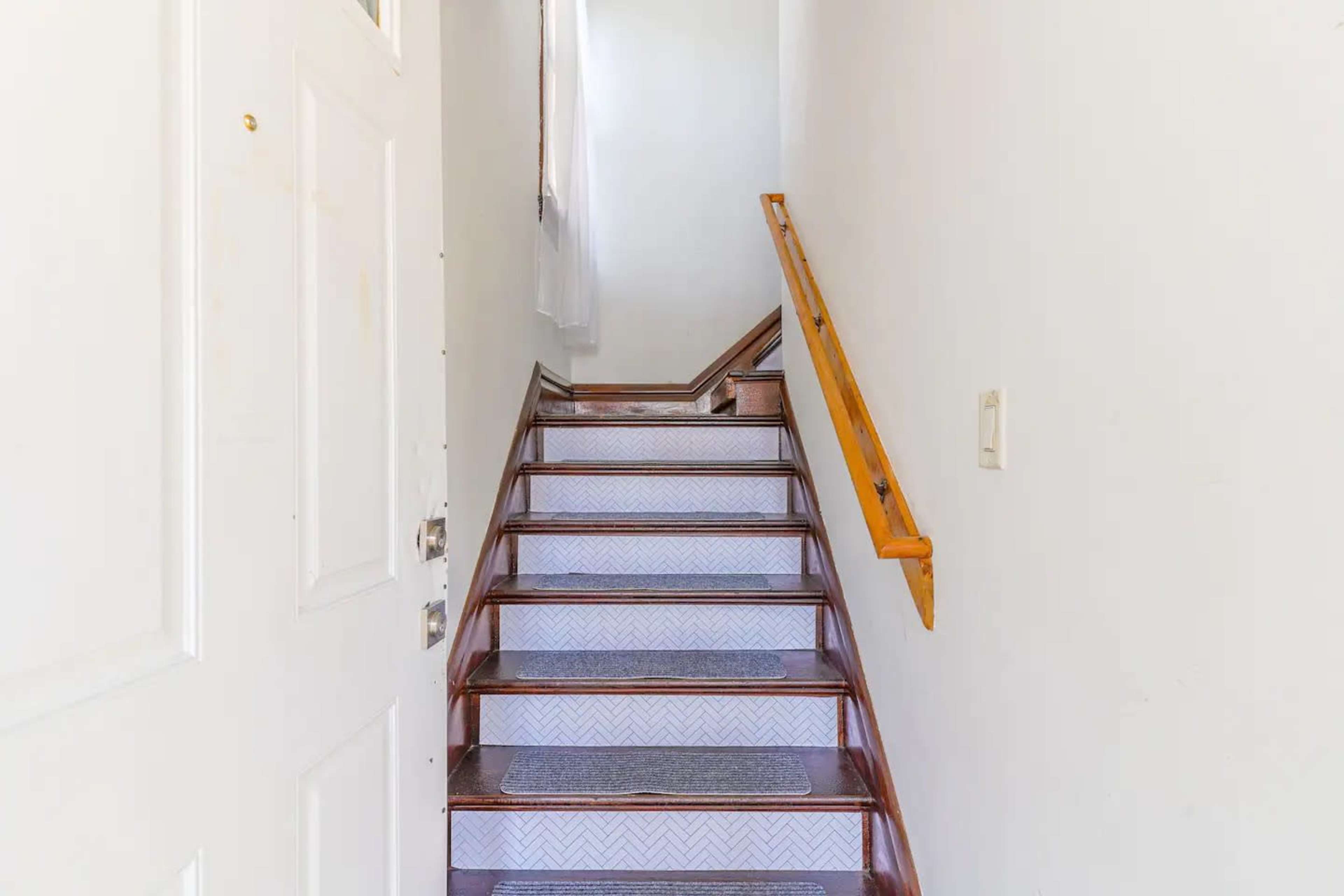 A staircase with wooden steps and a railing leads up to a brightly lit hallway.