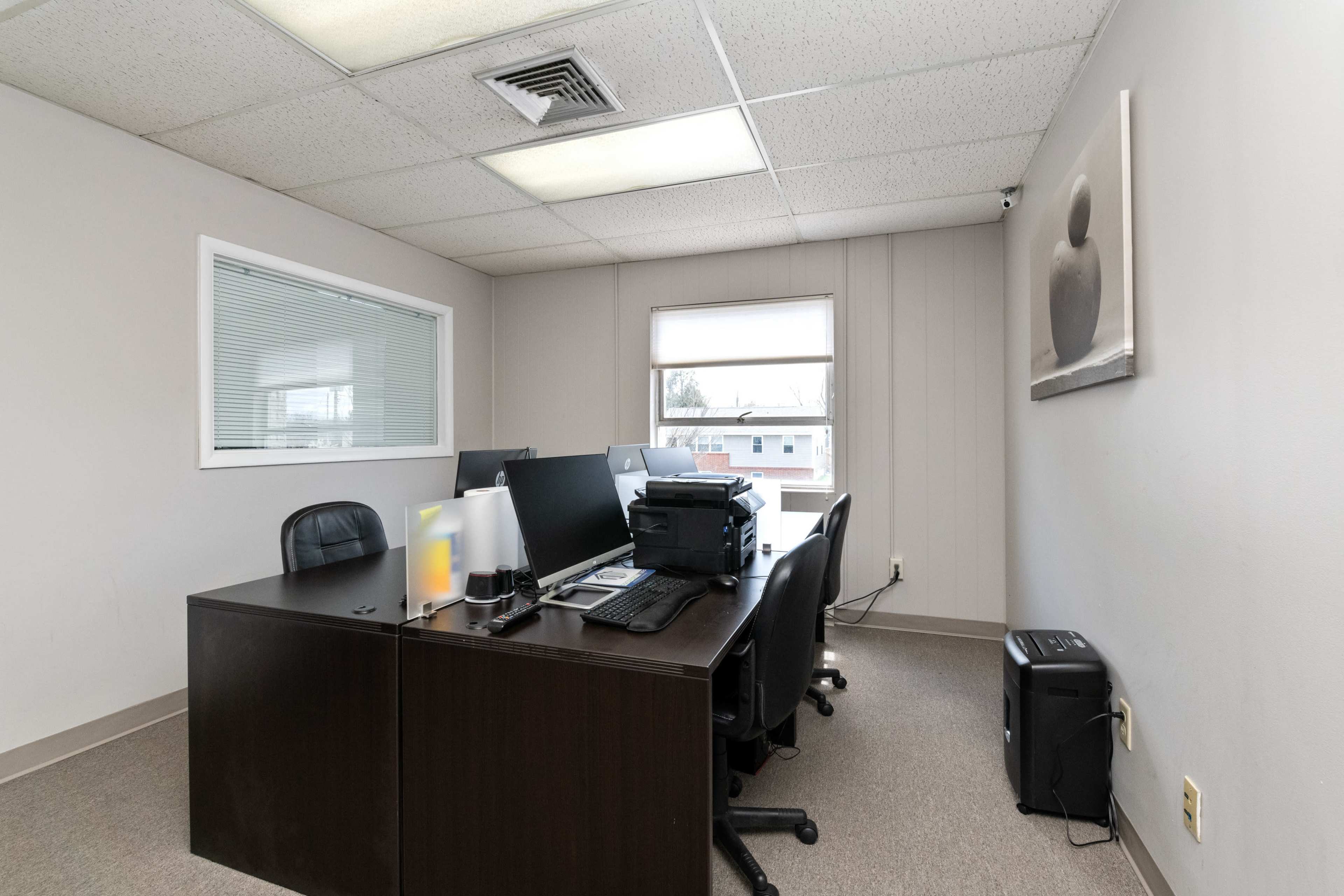 A small office space with a dark wood desk, multiple computer monitors, and minimal furnishings.