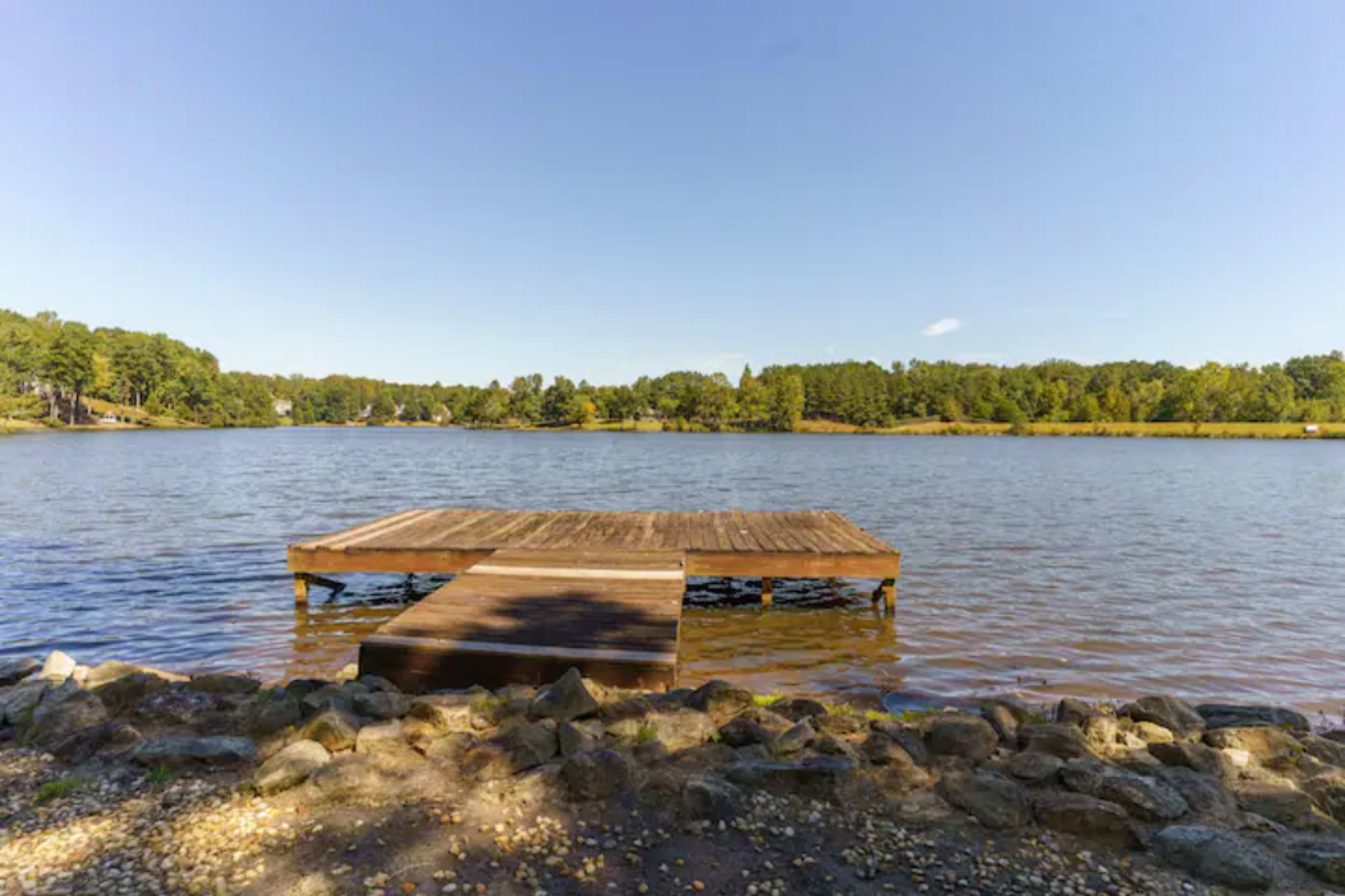 A wooden dock extends into a calm lake surrounded by trees under a clear blue sky.