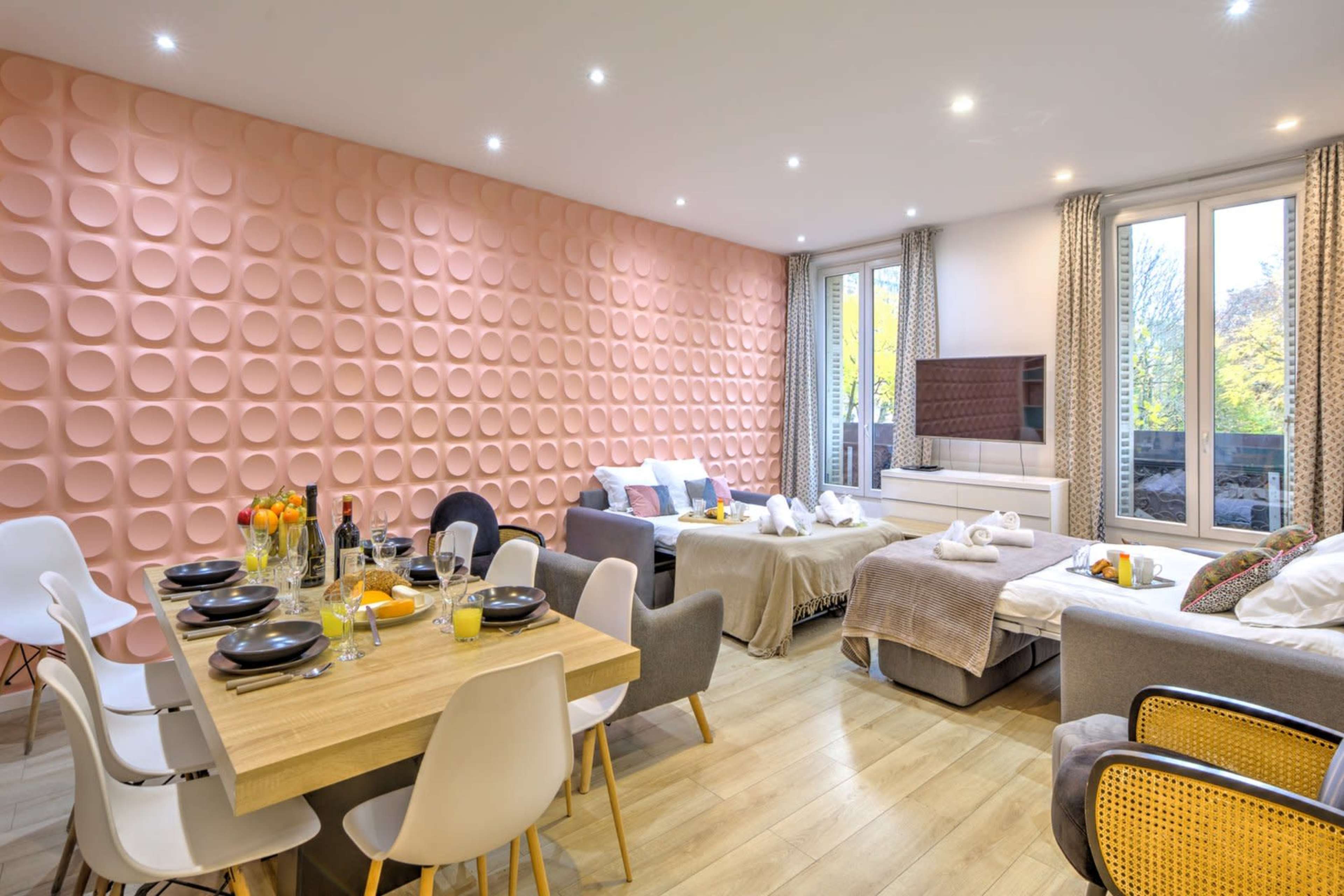 A spacious living area features a pink textured wall, dining table set for several guests, and comfortable seating arrangements.