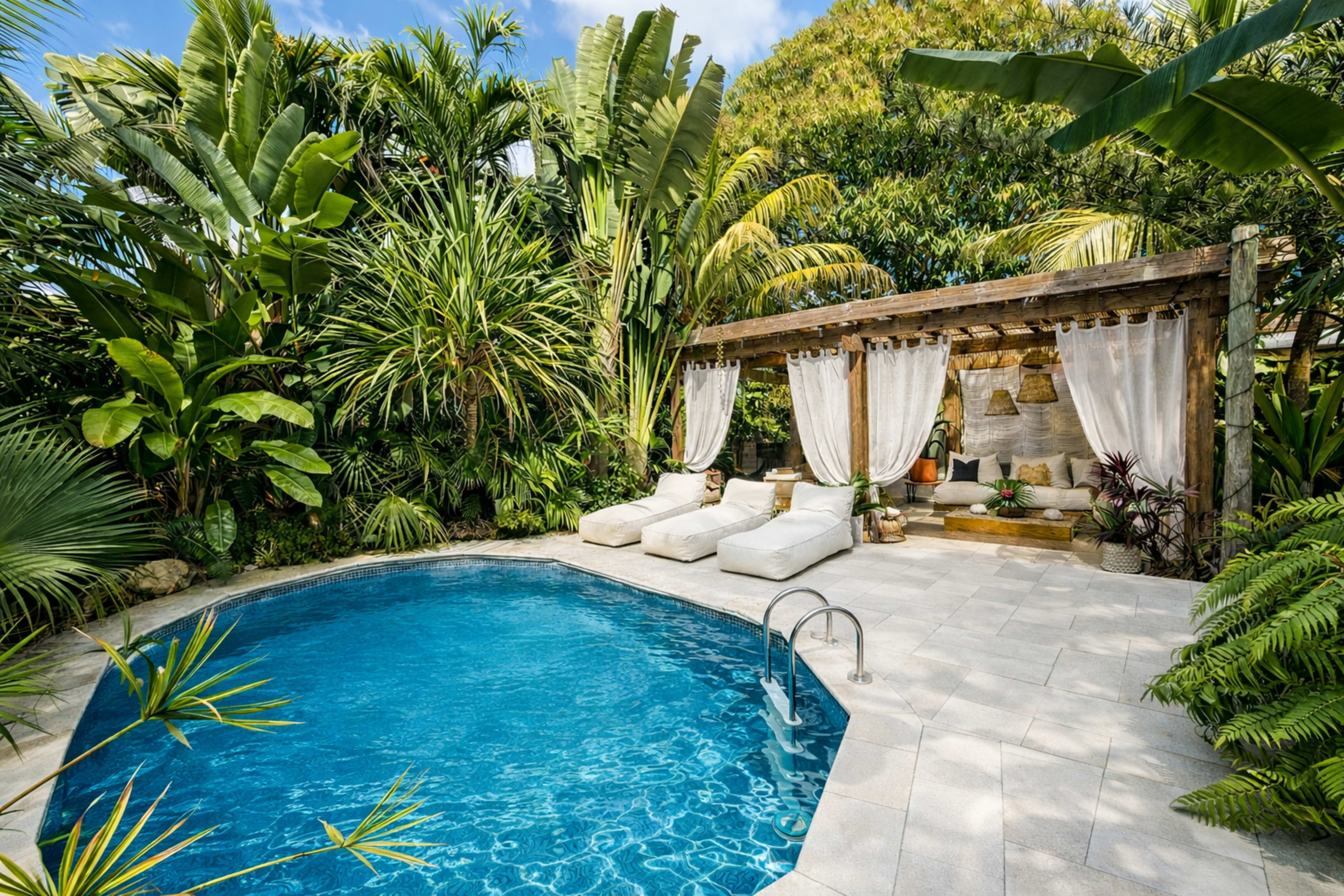 The image shows a small, private pool surrounded by lush tropical greenery and white sun loungers.