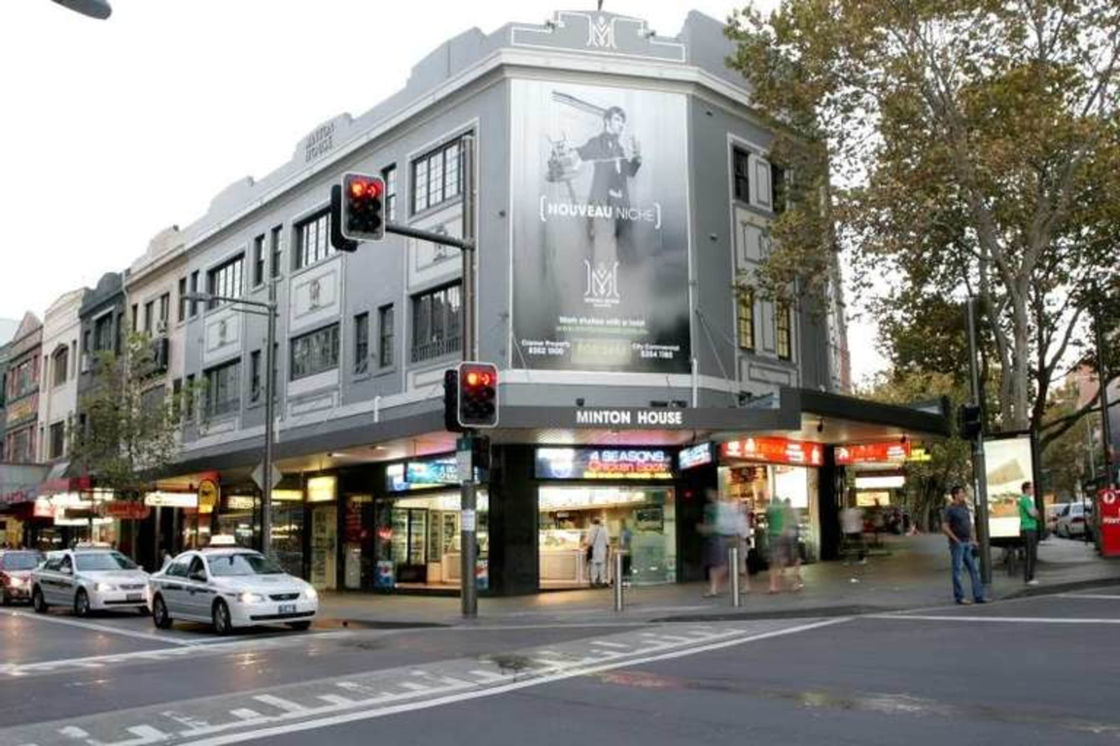 A multi-storey building with a large advertisement is located at a busy street intersection, featuring traffic signals and pedestrian activity.