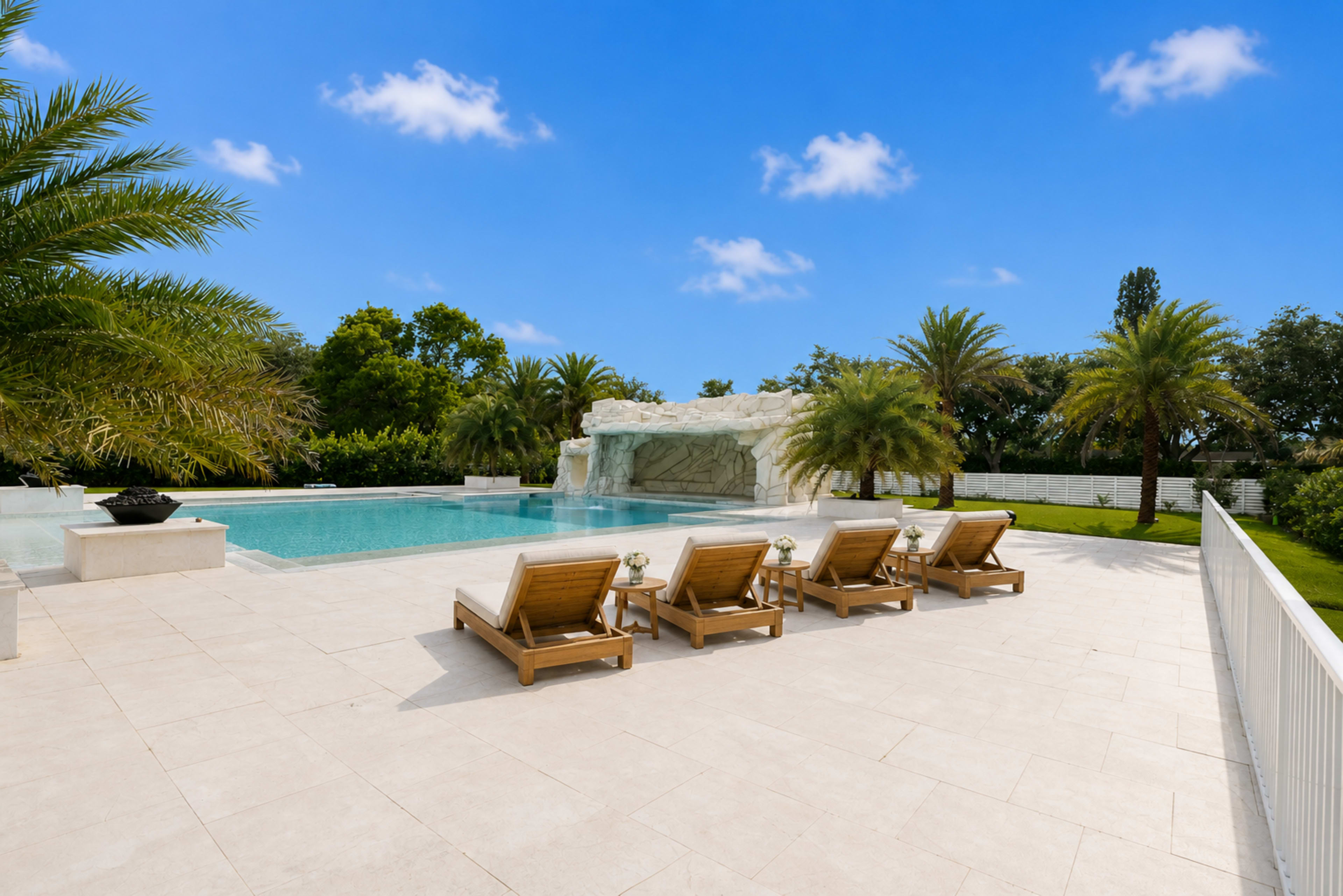 The image shows a well-maintained outdoor pool area with four lounge chairs positioned beside a clear pool and a decorative rock formation in the background.