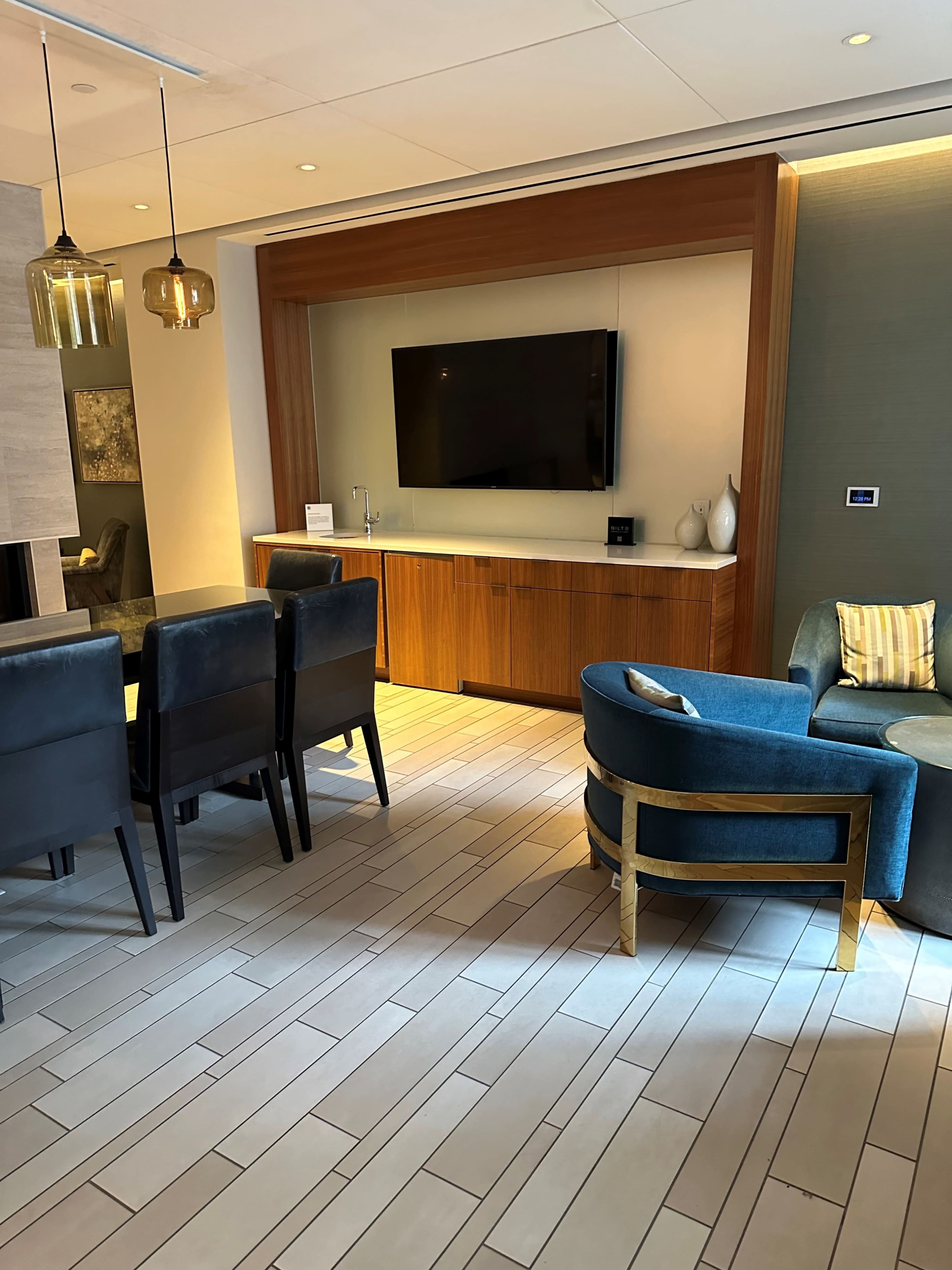 The image shows a modern living space featuring a dining area with a dark wooden table and chairs, a TV mounted on a wooden panel, and a blue upholstered armchair near the wall.